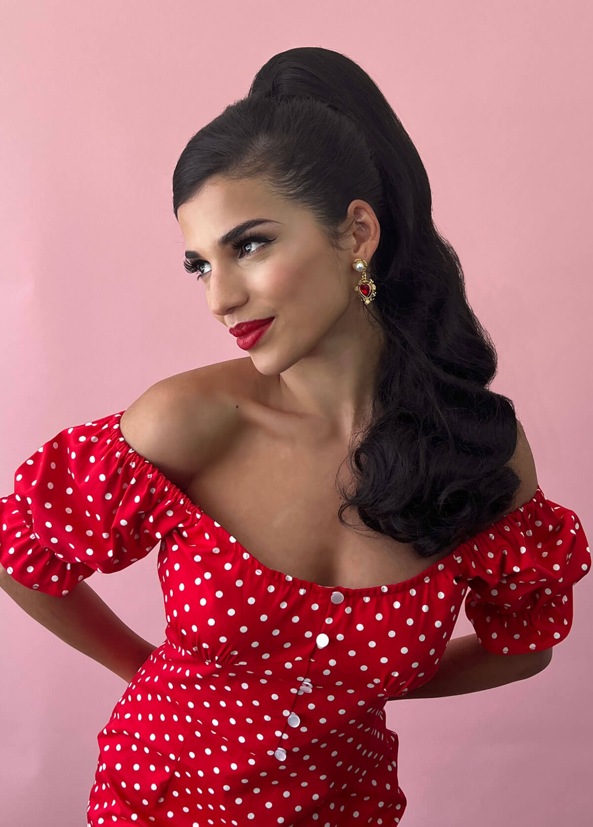 Woman wearing a red polka dot dress against a pink background. Retro style ponytail hairpiece, long with vintage waves: Arabella dark chocolate brown 6