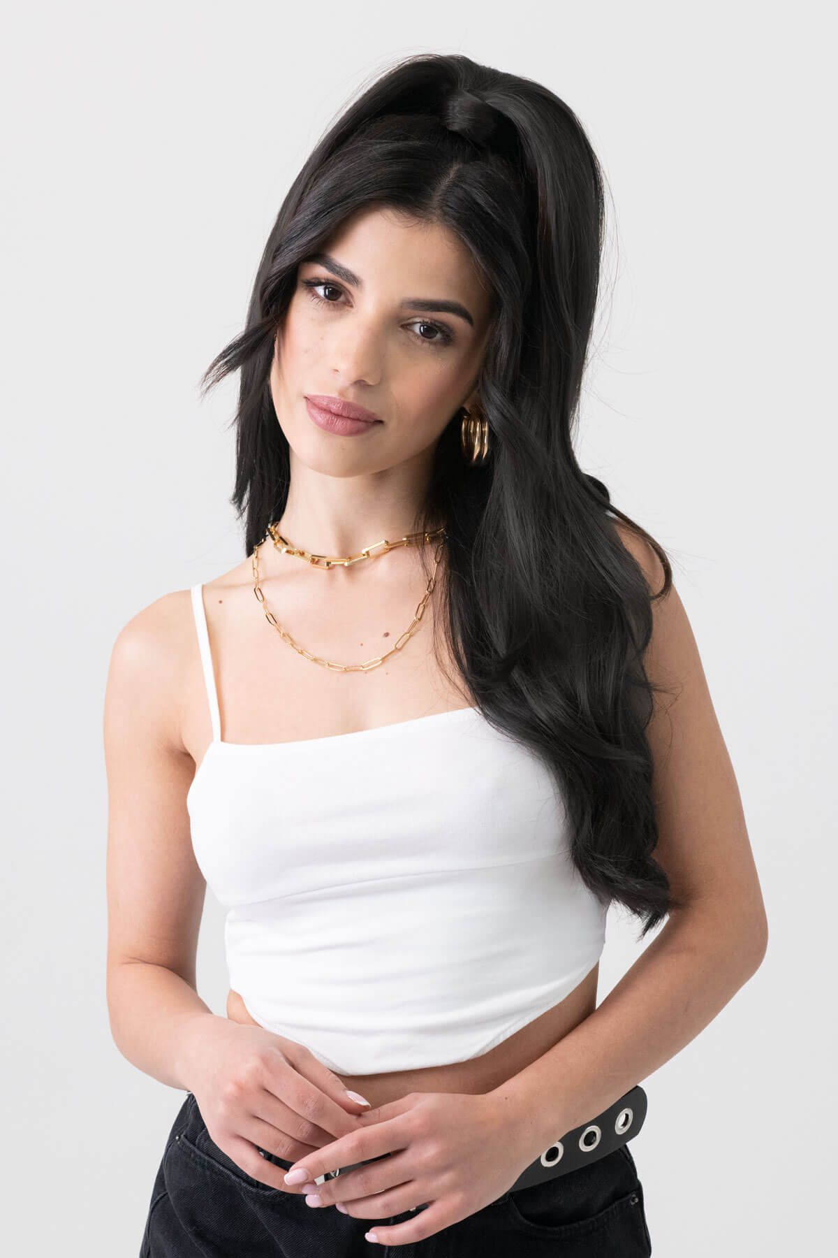 Woman wearing a white top and black pants with a plain background. Long sleek ponytail extension with gentle, layered waves: Mali dark brown 4