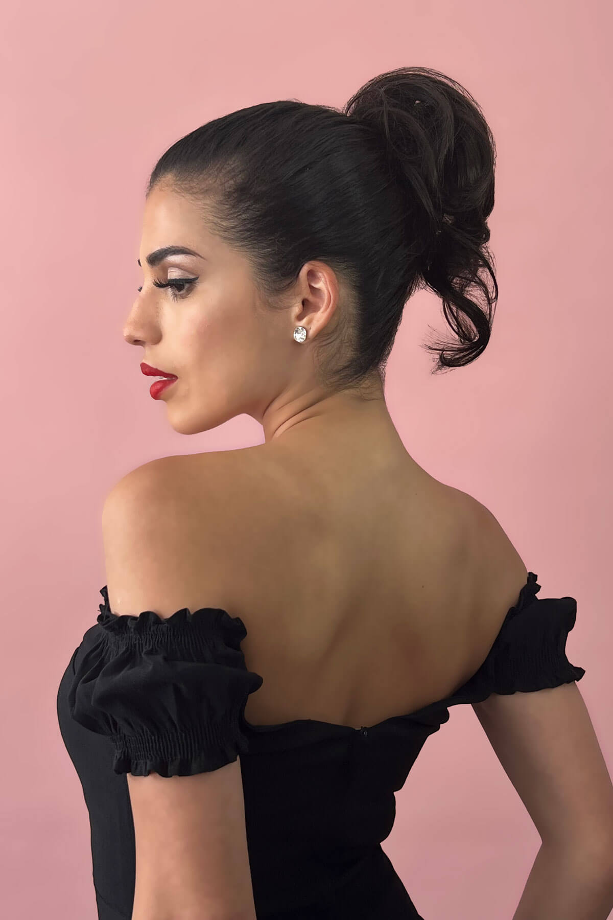 Woman in a black off-shoulder dress with red lipstick against a pink background. Short ponytail extension hairpiece, short with whisps: Leah