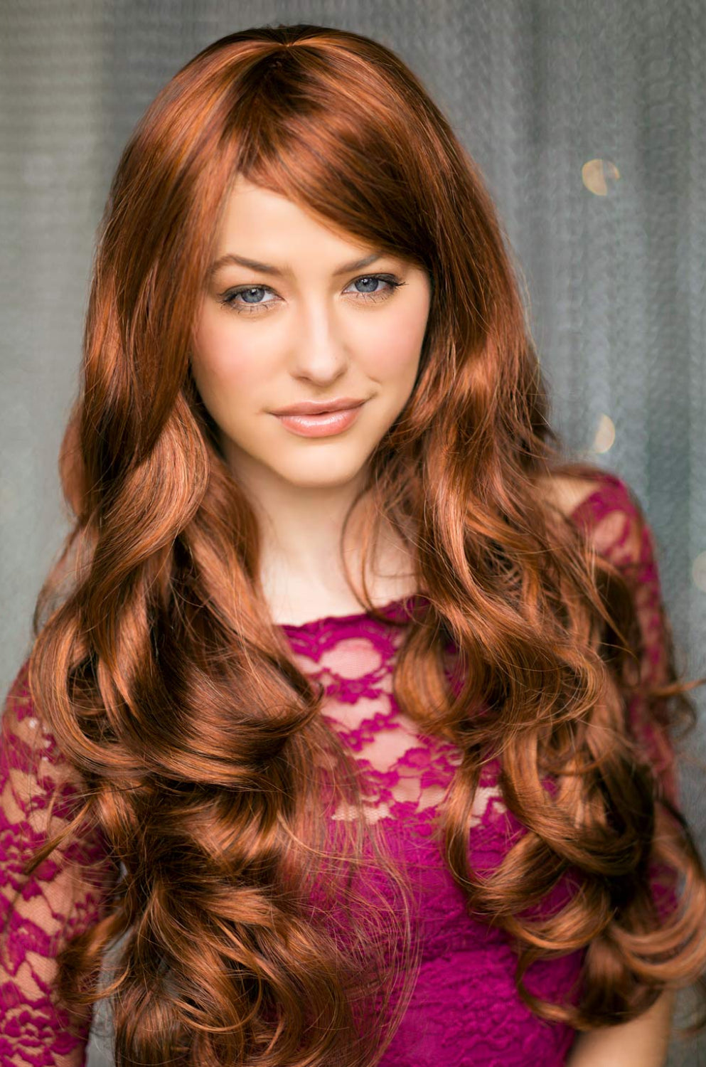A person wearing a red and auburn wig with blonde highlights, featuring long bouncing curls and waves with a side sweeping fringe. Red & auburn wig with blonde highlights, long: Freya