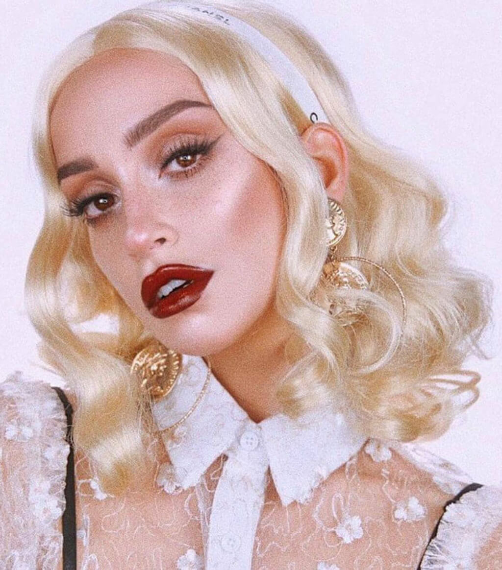 Person with blonde hair and red lipstick wearing a white lace top. 40s blonde pinup style wig with marcel waves: Lauren