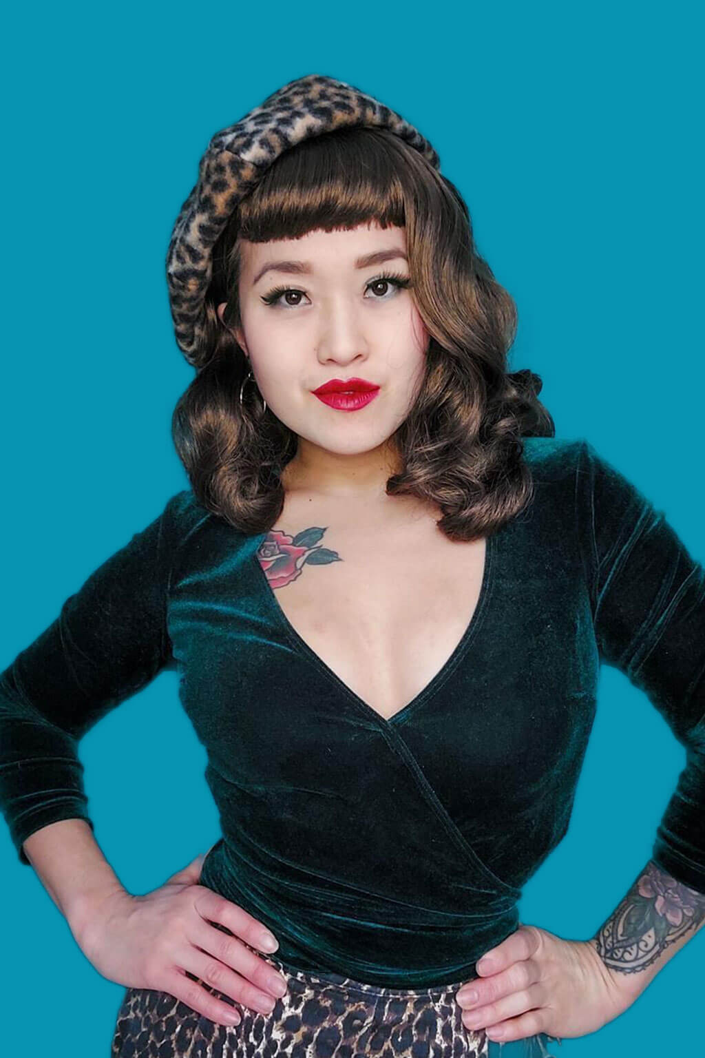 Woman wearing a green velvet top and leopard print headband against a blue background. Brown pinup style wig, curled with short fringe: Carolina mocha brown 10