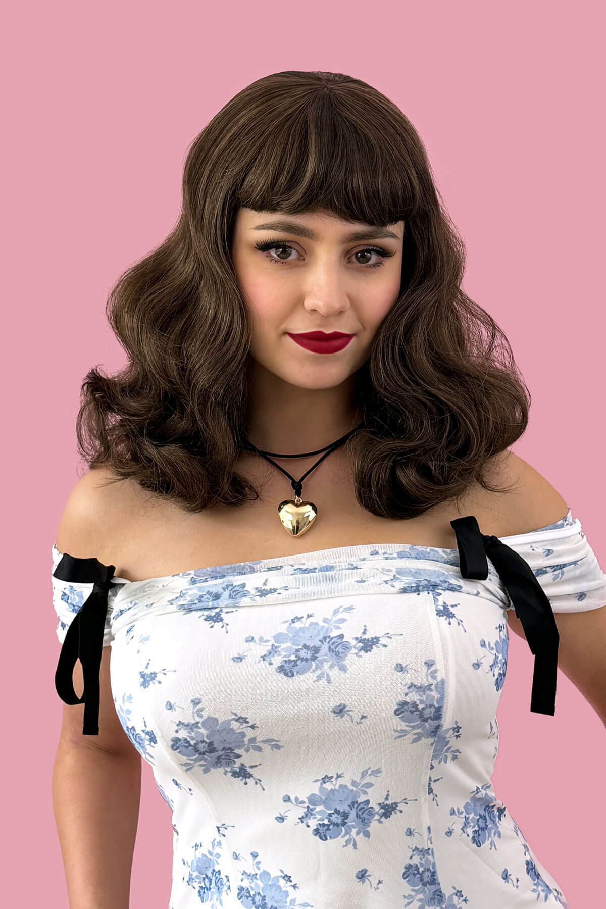 Woman with vintage-style hair and dress against a pink background. brown pinup style wig, curled with short fringe: Carolina Brown and blonde 8H27