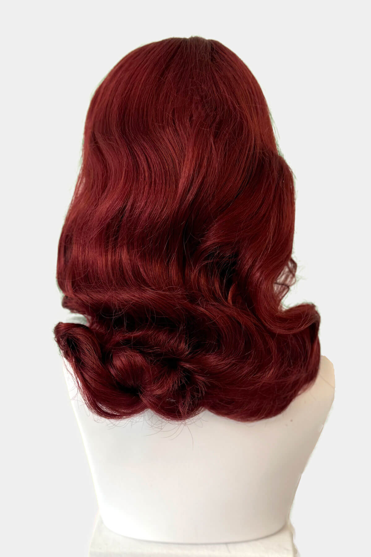 Red wig from behind on a mannequin head against a white background. Copper red 1950s pinup wig, curled with short fringe: Kitty