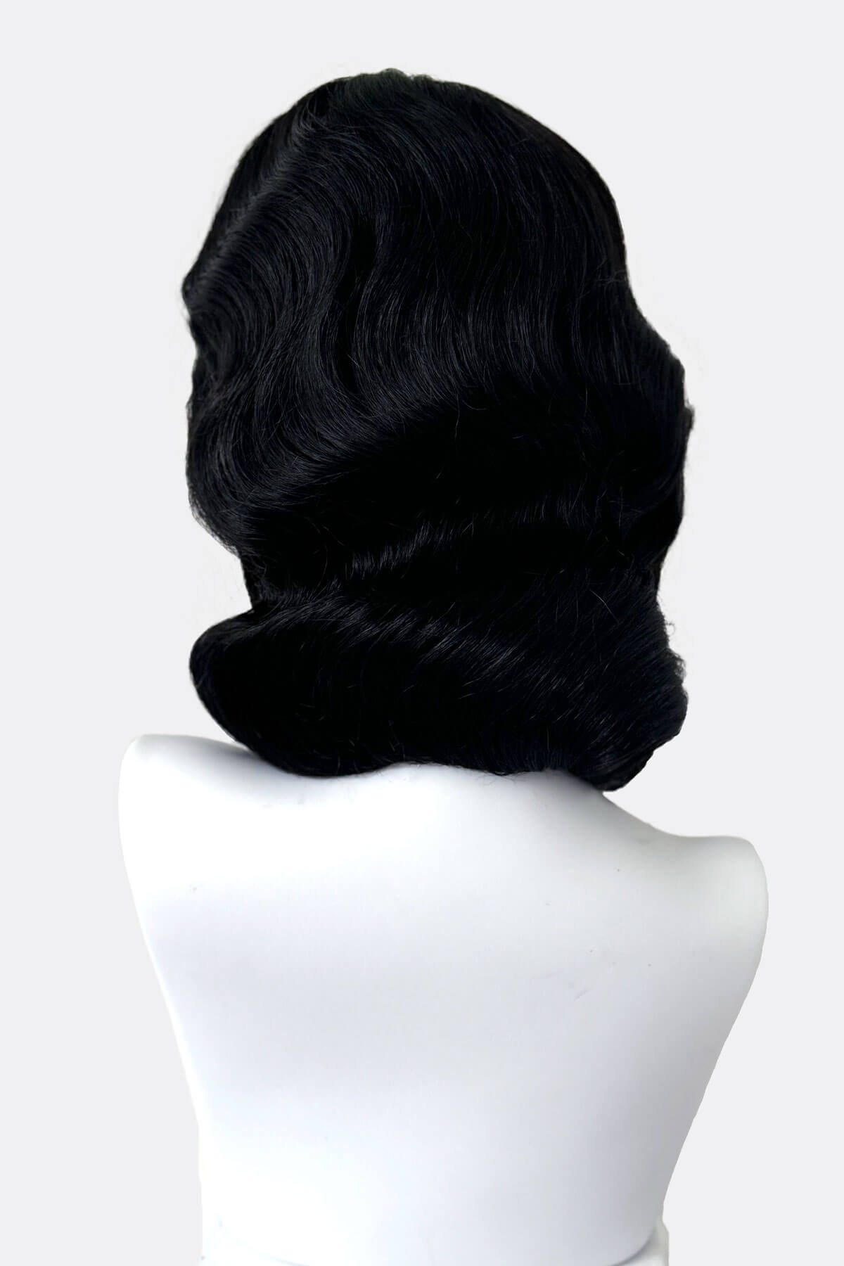 Black wig on a white mannequin head against a white background. Black 40s style wig with beautiful marcel waves: Dita