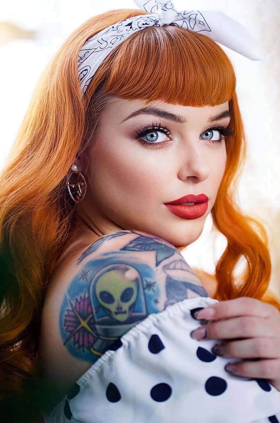 Woman with red hair and tattoos on her shoulder wearing a white polka dot dress. Ginger wig, pinup style with short fringe and gentle waves, 1950s style: Vida