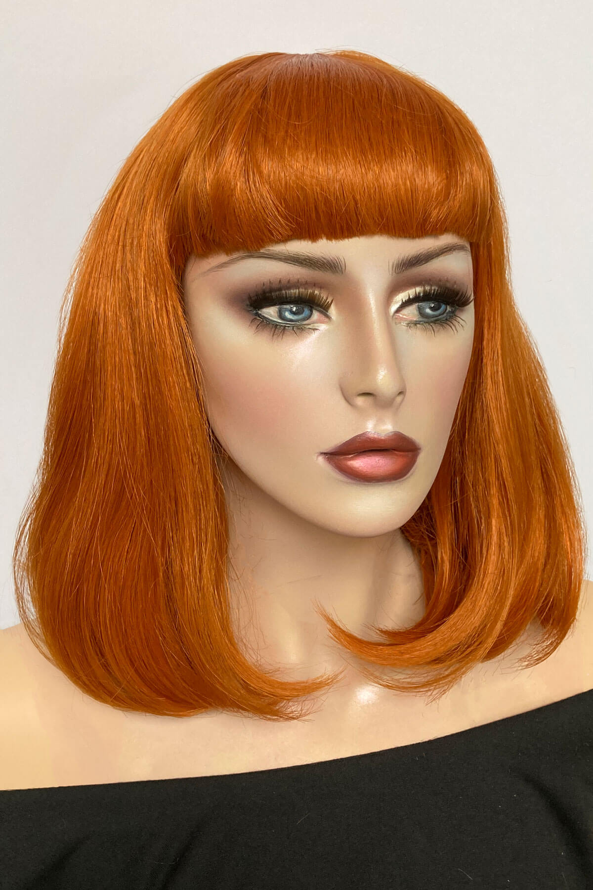 Mannequin head with orange wig and bangs on a plain background. Ginger long bob wig with a short retro style fringe: Bonnie