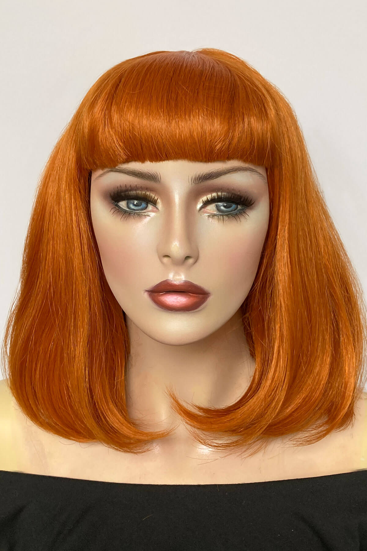 Mannequin head with orange wig on a white background. Ginger long bob wig with a short retro style fringe: Bonnie