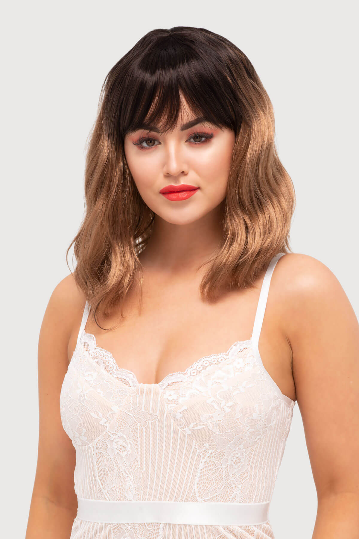 Woman wearing a white lace dress with a plain background. Long wavy bob wig, dark brown blending to light brown: Elodie