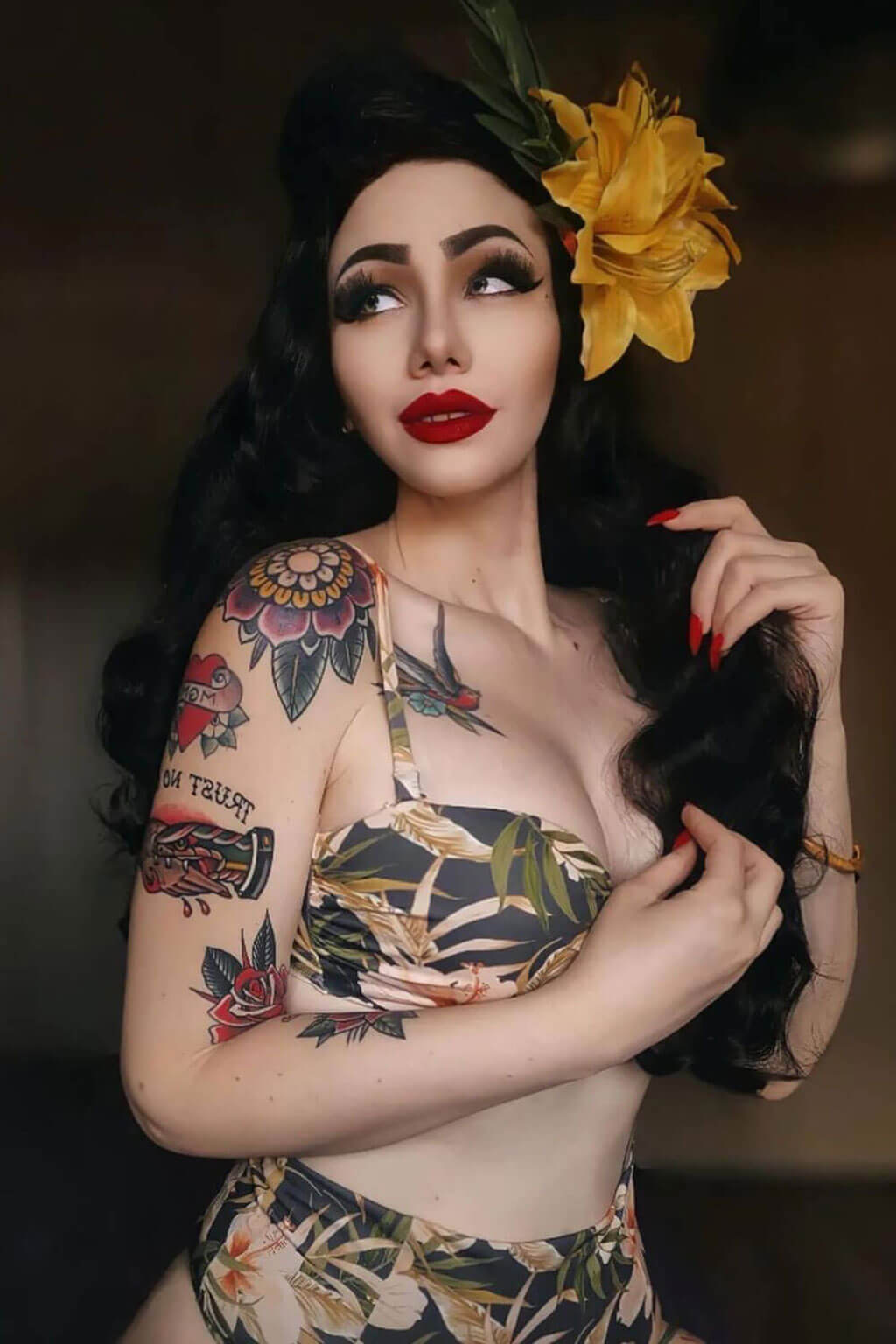 Woman with tattoos and floral headpiece posing against a dark background. Long black pinup style wig with vintage hollywood waves: Veronica
