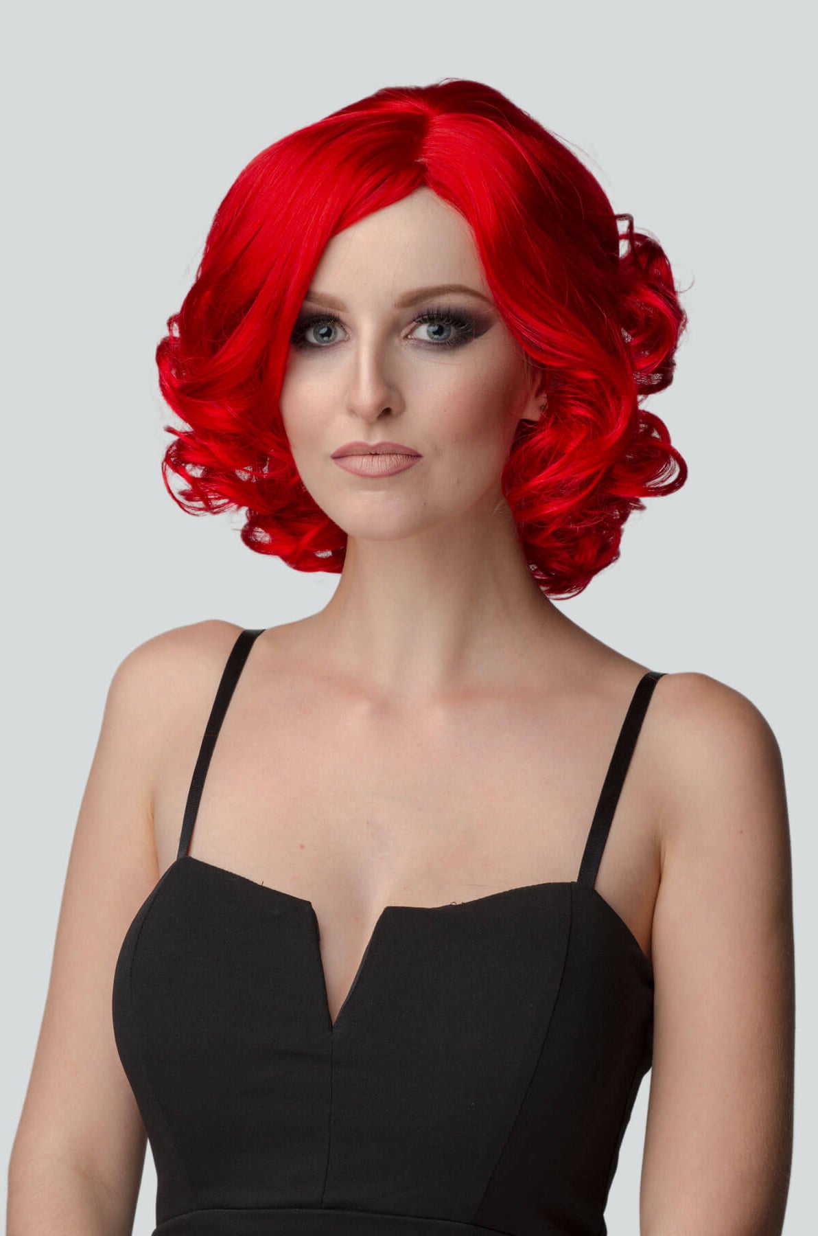 Woman with red wig and black dress on gray background. Rihanna style red wig, short with curls: Rihanna