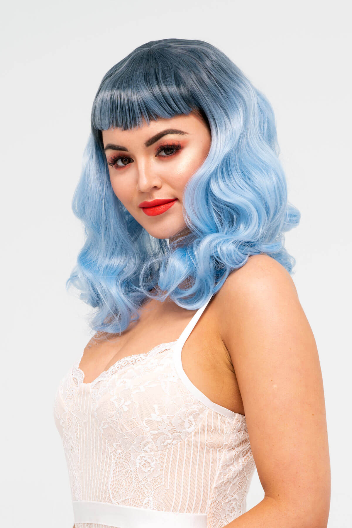 Woman with blue wig and red lipstick on a white background. Black and blue pinup style wig, curled with short fringe, 1950s style: Luna