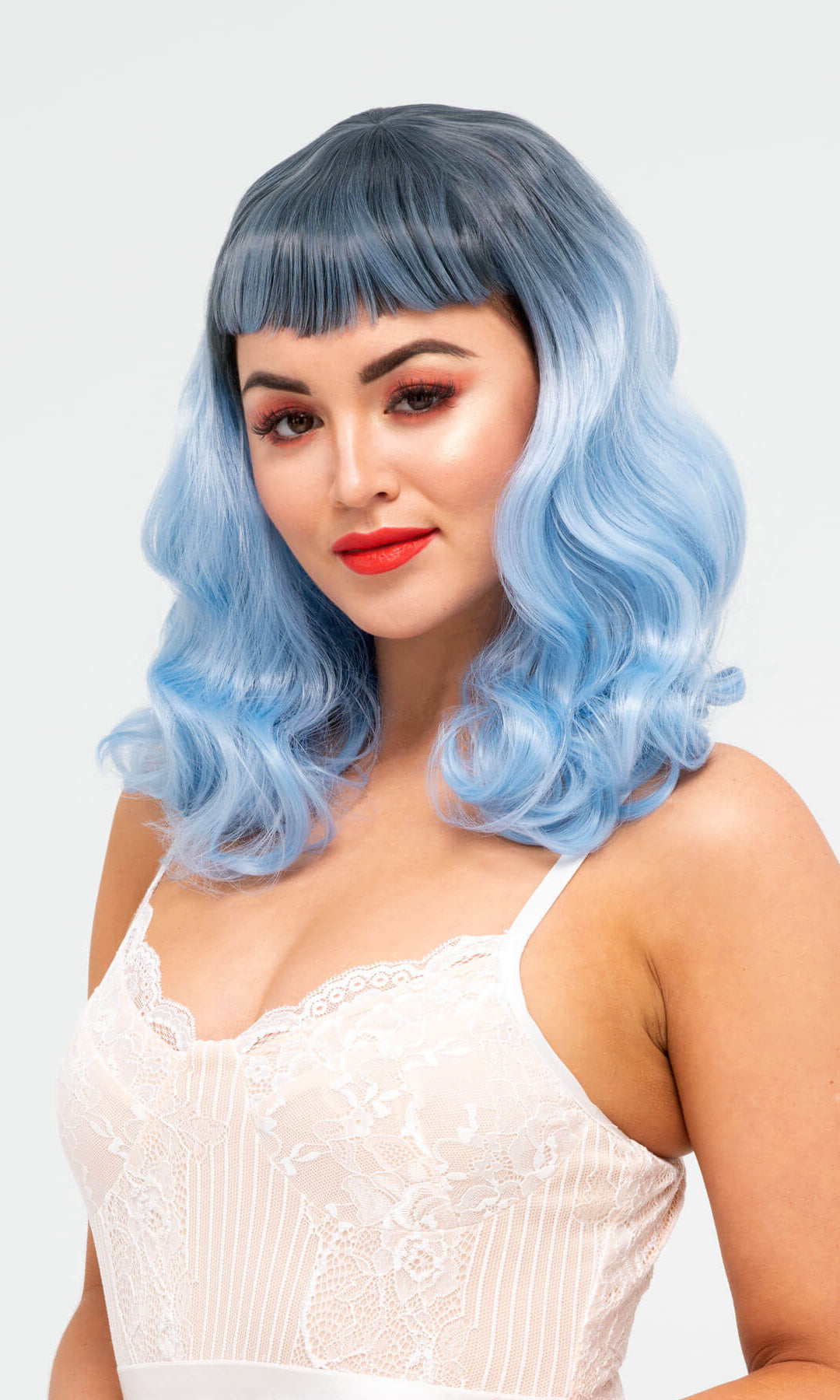 Woman with blue wig and red lipstick on a white background. Black and blue pinup style wig, curled with short fringe, 1950s style: Luna