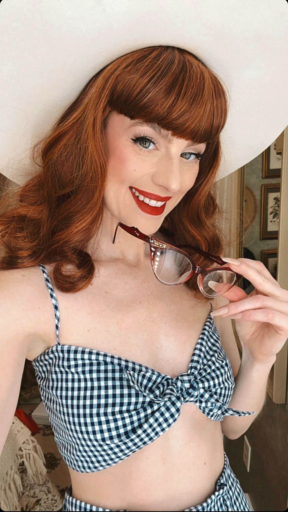 Woman wearing a checkered bikini holding sunglasses indoors. Auburn pinup style wig, finger waved with short fringe, 1950s style: Heidi