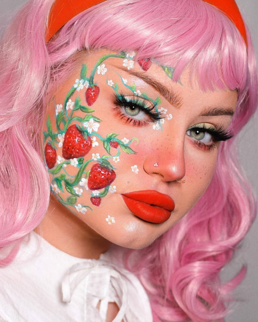 Person with pink hair and strawberry design on face. Pink pinup style wig, with finger waves and a short fringe, 1950s style: Stevie