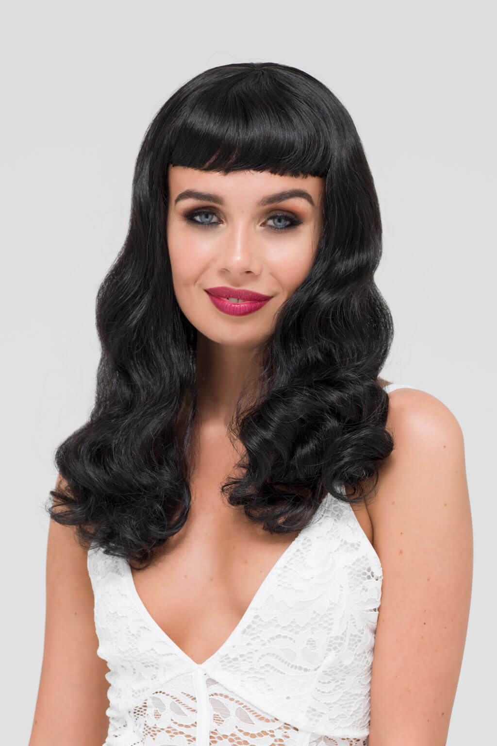 Woman with a stylish black wig and white lace top on a plain background - Black 1950s pinup style wig, curled with short fringe: Milena