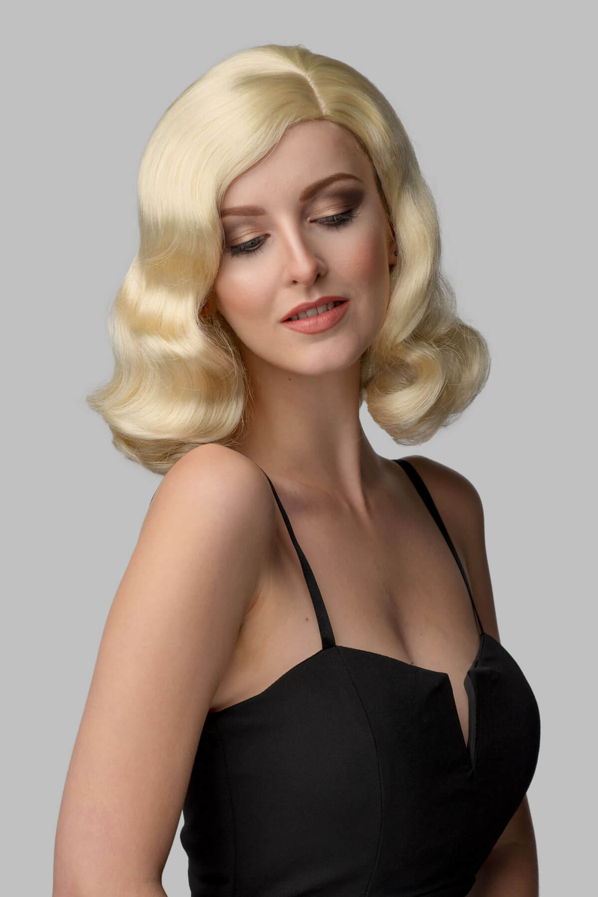 Woman with a blonde wig styled in vintage fashion against a gray background. 40s blonde pinup style wig with marcel waves: Lauren