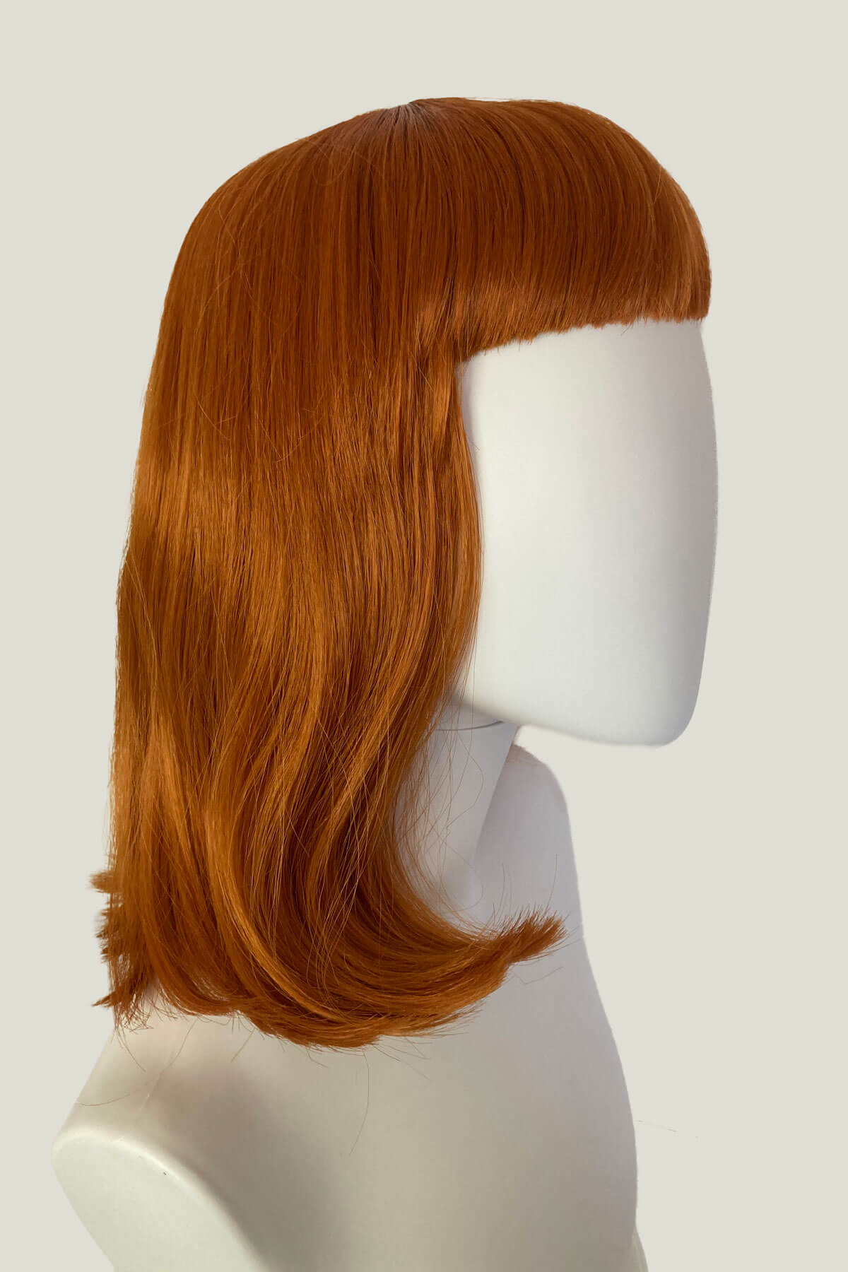 Red wig on a mannequin head against a white background. Ginger long bob wig with a short retro style fringe: Bonnie