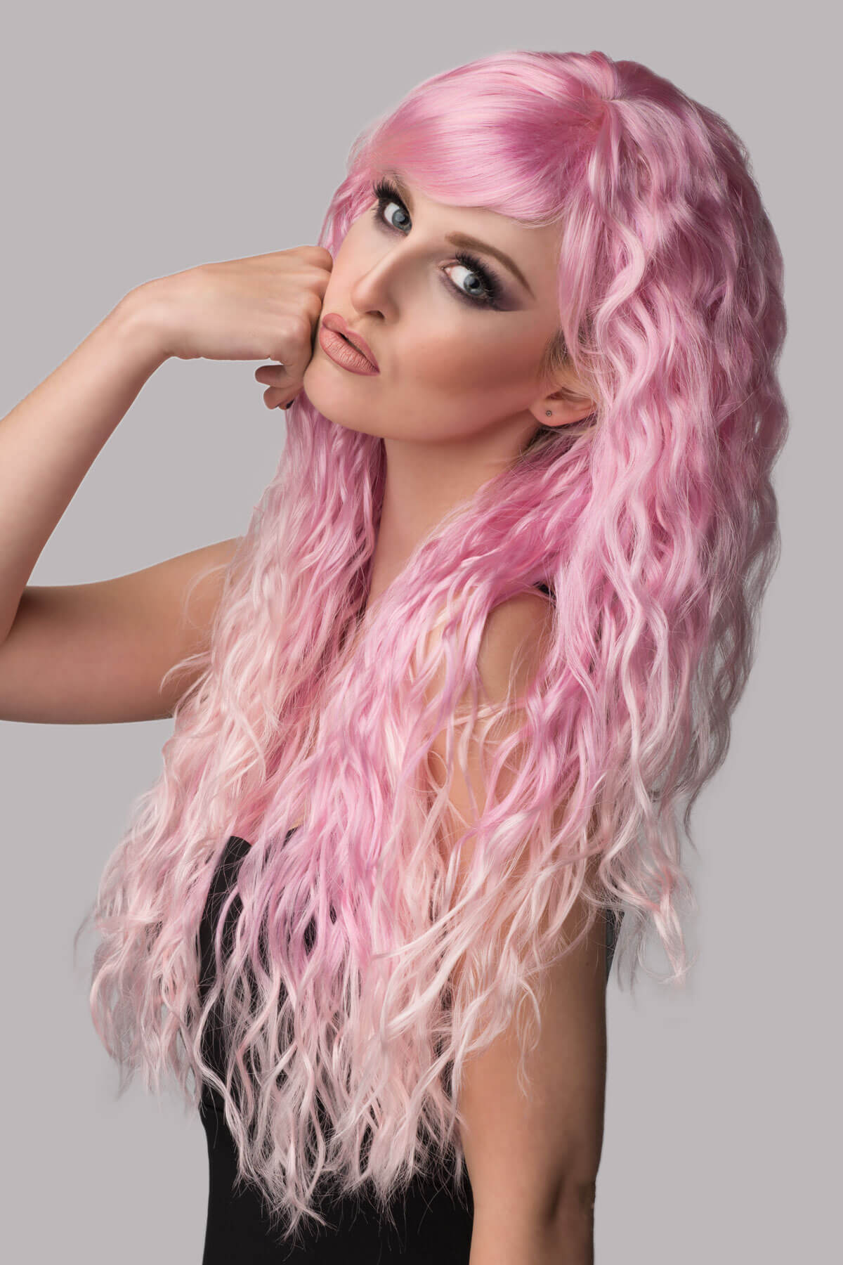 Woman with pink and white wig posing against a gray background. Crimped pink wig, long, in two colour pink ombre: Peony