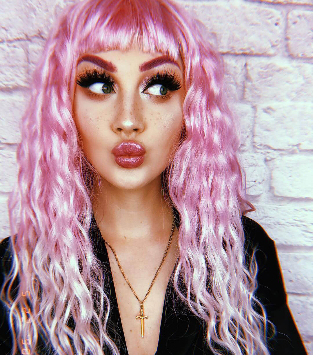 Person with pink hair and dramatic makeup against a brick wall.