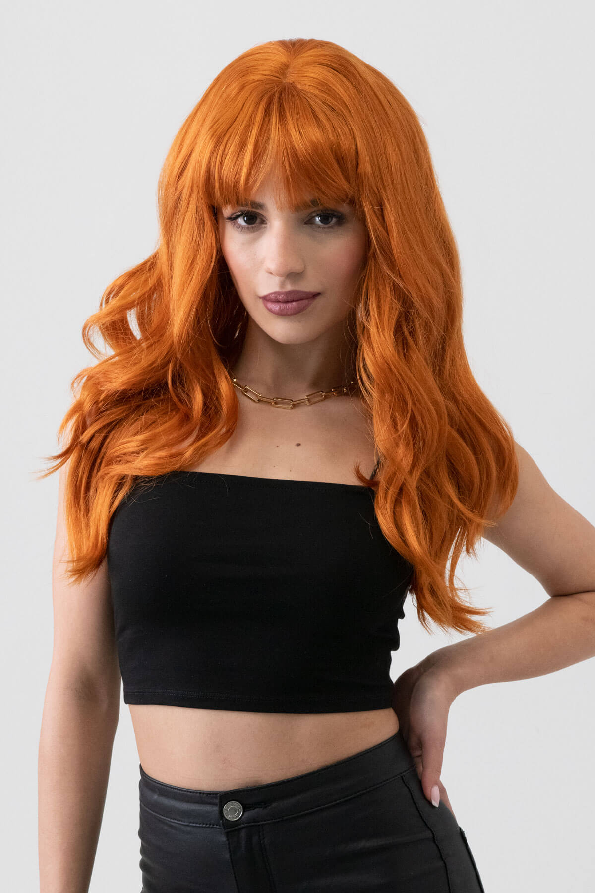 Person with long orange hair wearing a black top and black pants on a white background. Long ginger wig with cascading waves: Davina