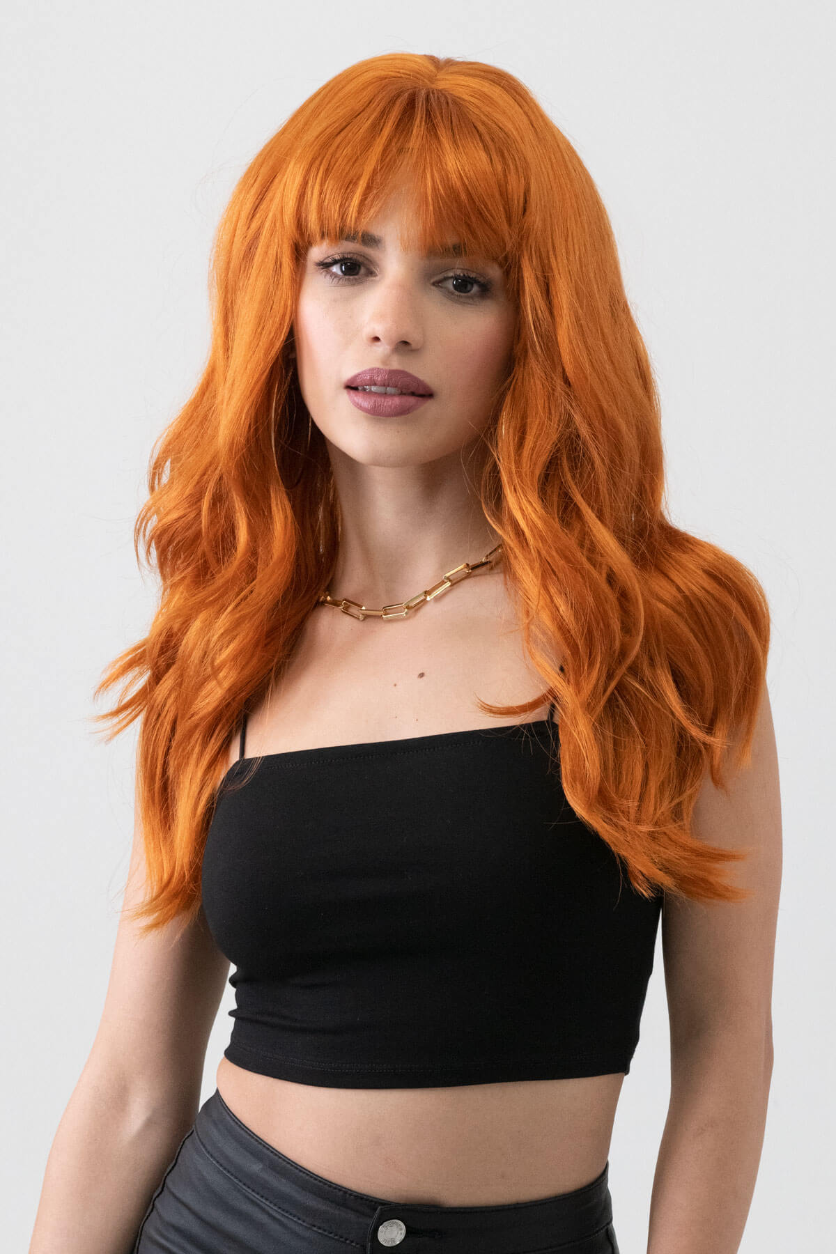 Woman with vibrant orange hair wearing a black top against a plain background. Long ginger wig with cascading waves: Davina