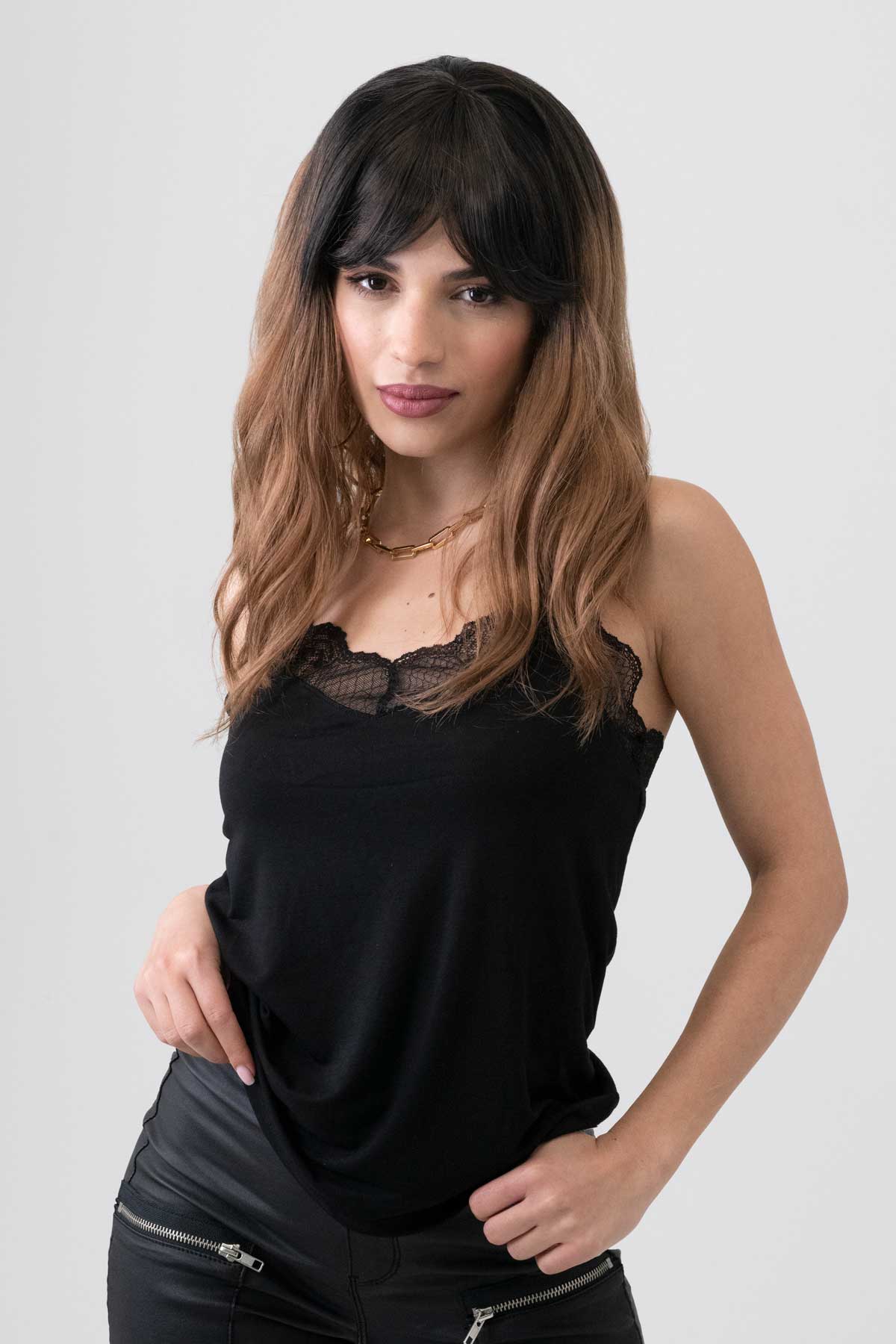 Woman wearing a black sleeveless top with lace details on a white background. Long wavy bob wig (lob), dark brown to light brown ombre: Rowena