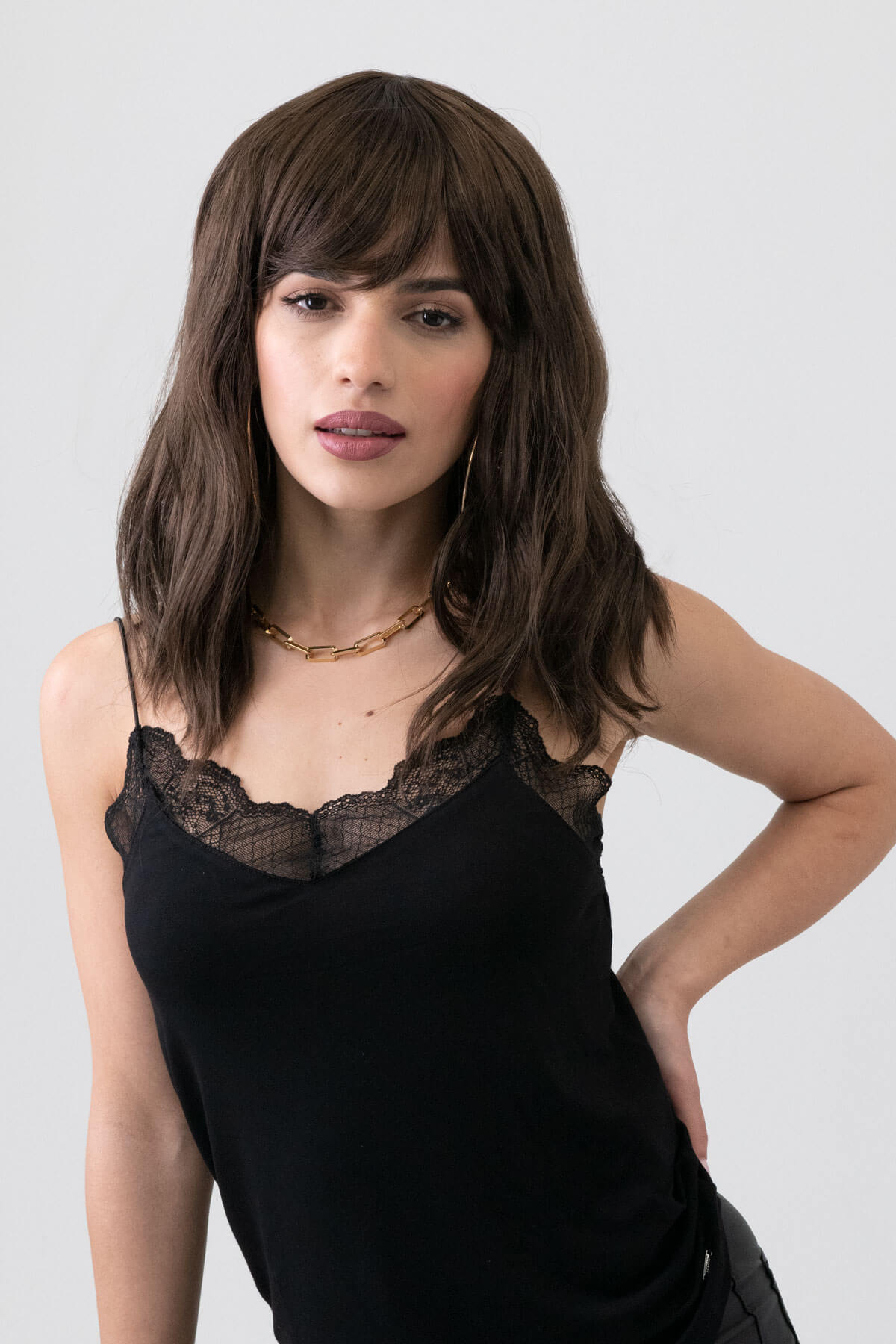Woman wearing a black lace top against a plain background. Long brown wavy bob (lob) wig: Lottie