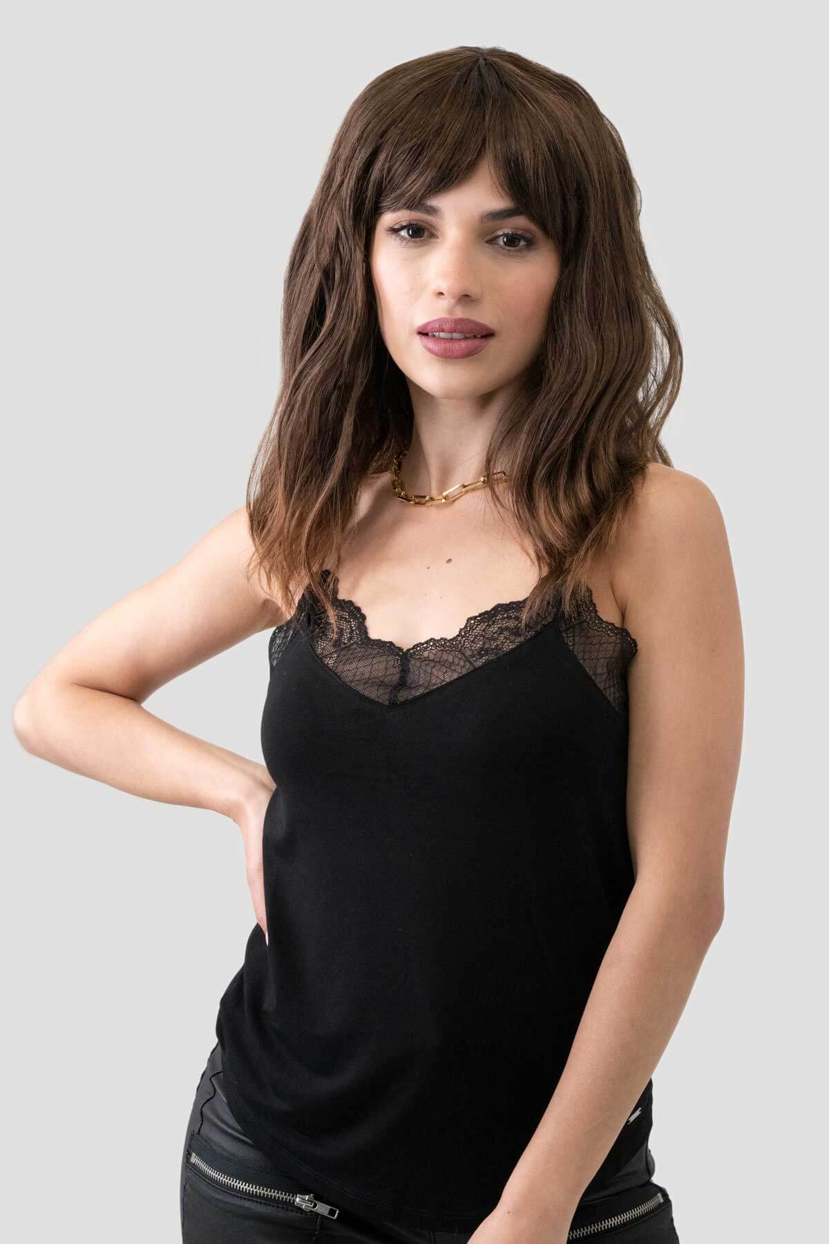 Woman wearing a black lace-trimmed top on a gray background. Brown long wavy bob (lob) wig with highlights: Melanie