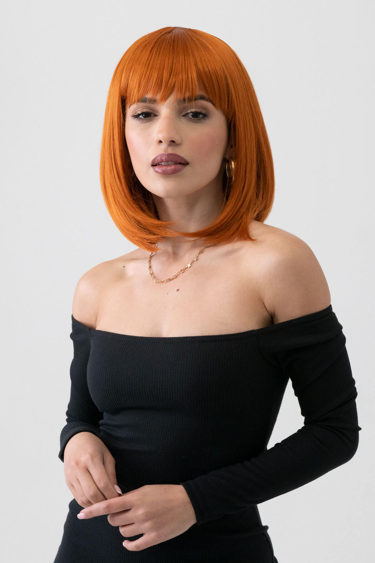 Woman with orange hair wearing a black off-shoulder top on a white background. Ginger bob wig, shoulder length: Ember