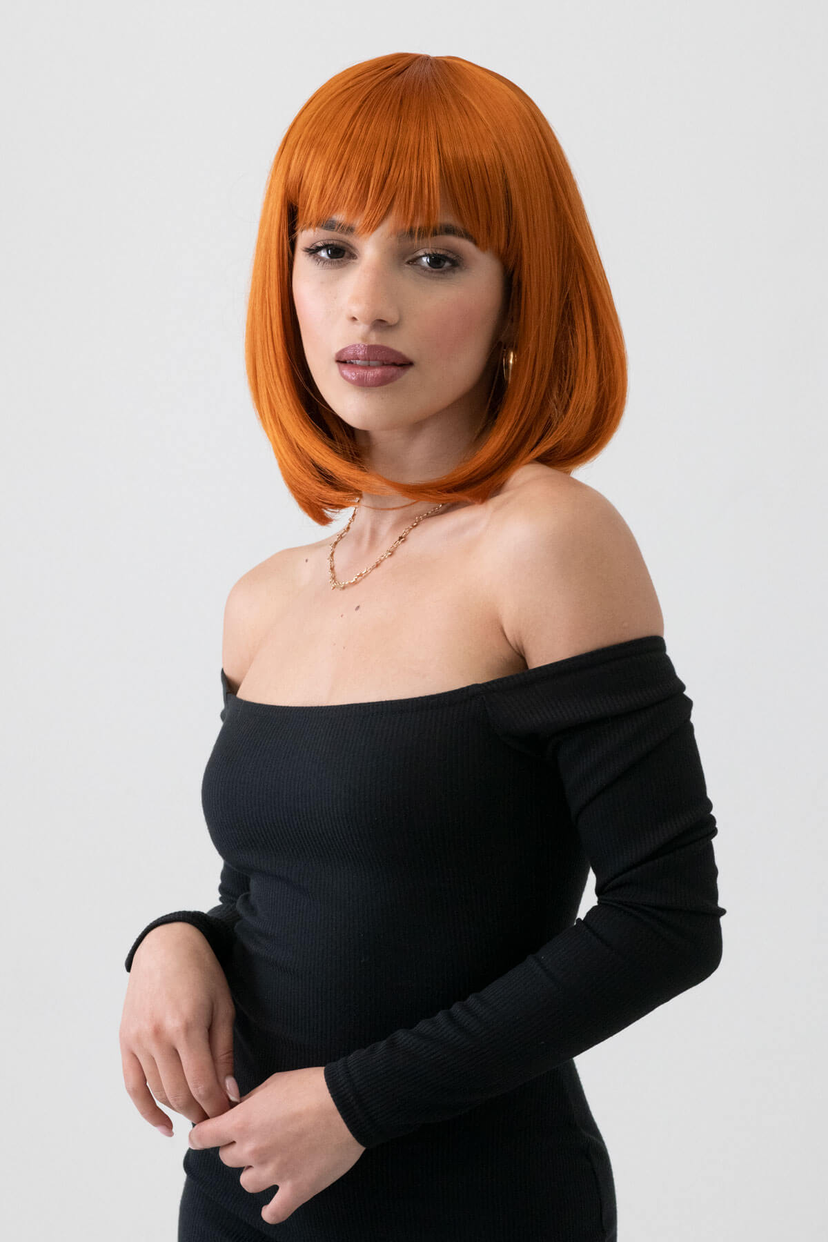 Woman with orange hair wearing a black off-shoulder top against a white background. Ginger bob wig, shoulder length: Ember