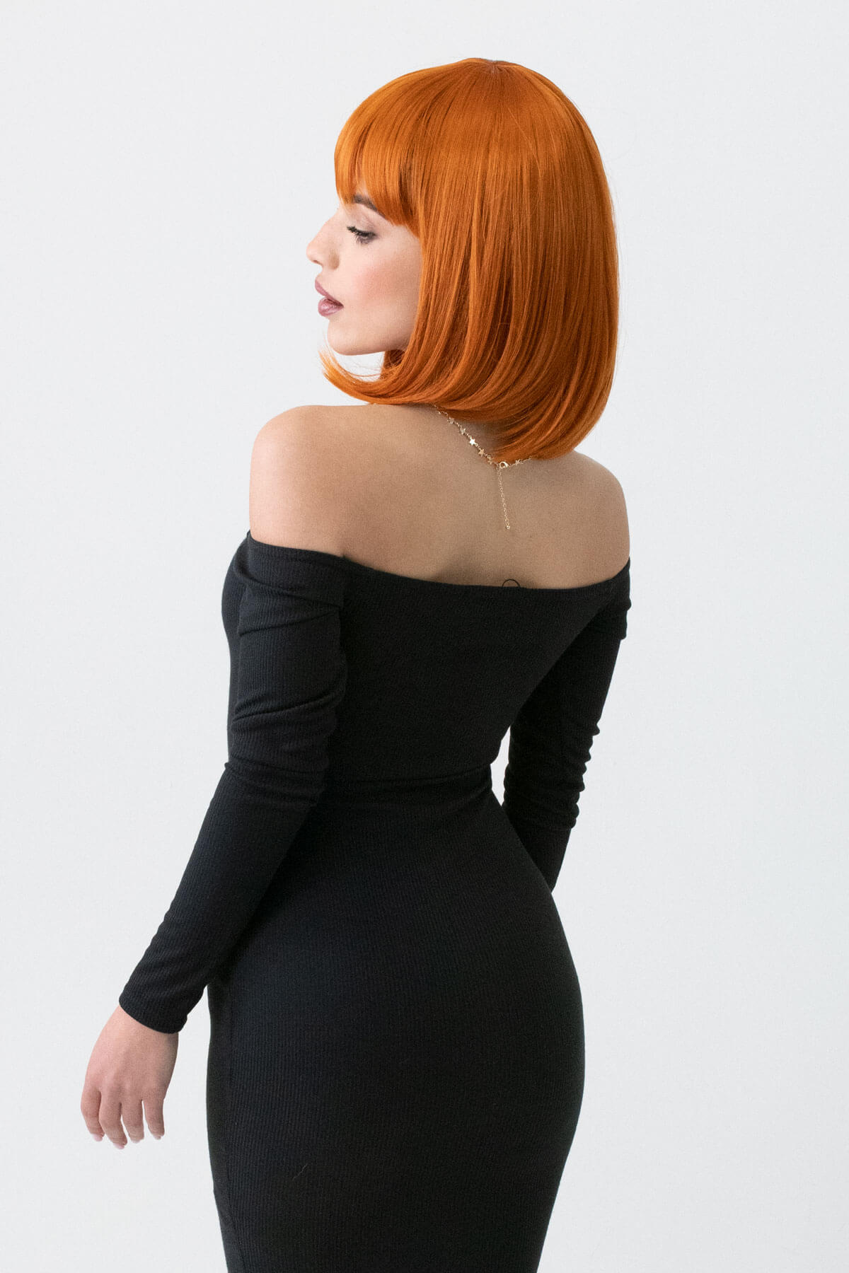 Woman with red hair wearing a black off-shoulder dress against a white background. Ginger bob wig, shoulder length: Ember