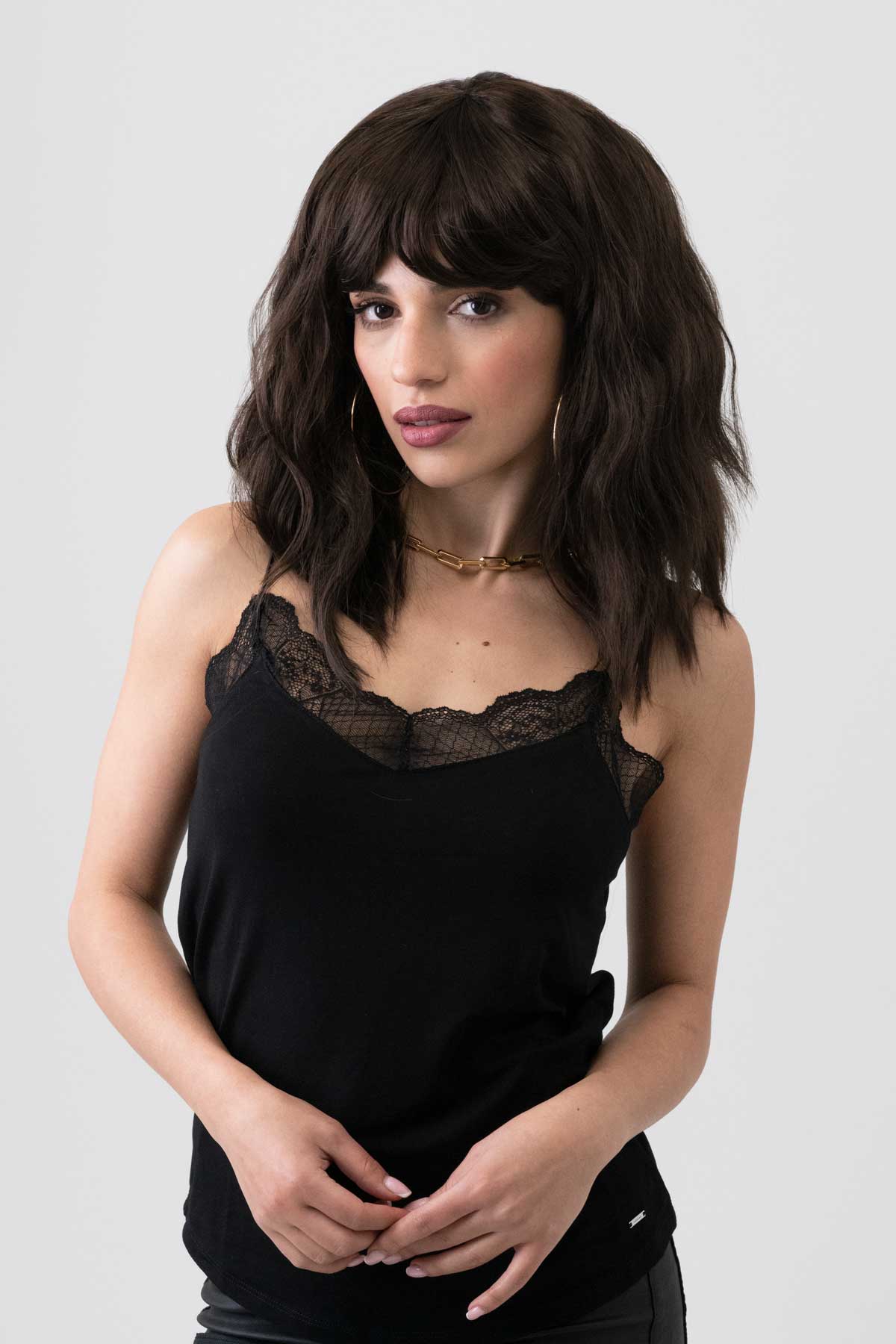 Woman wearing a black tank top with lace detail on a plain background. Dark chocolate brown long wavy bob wig: Roxy