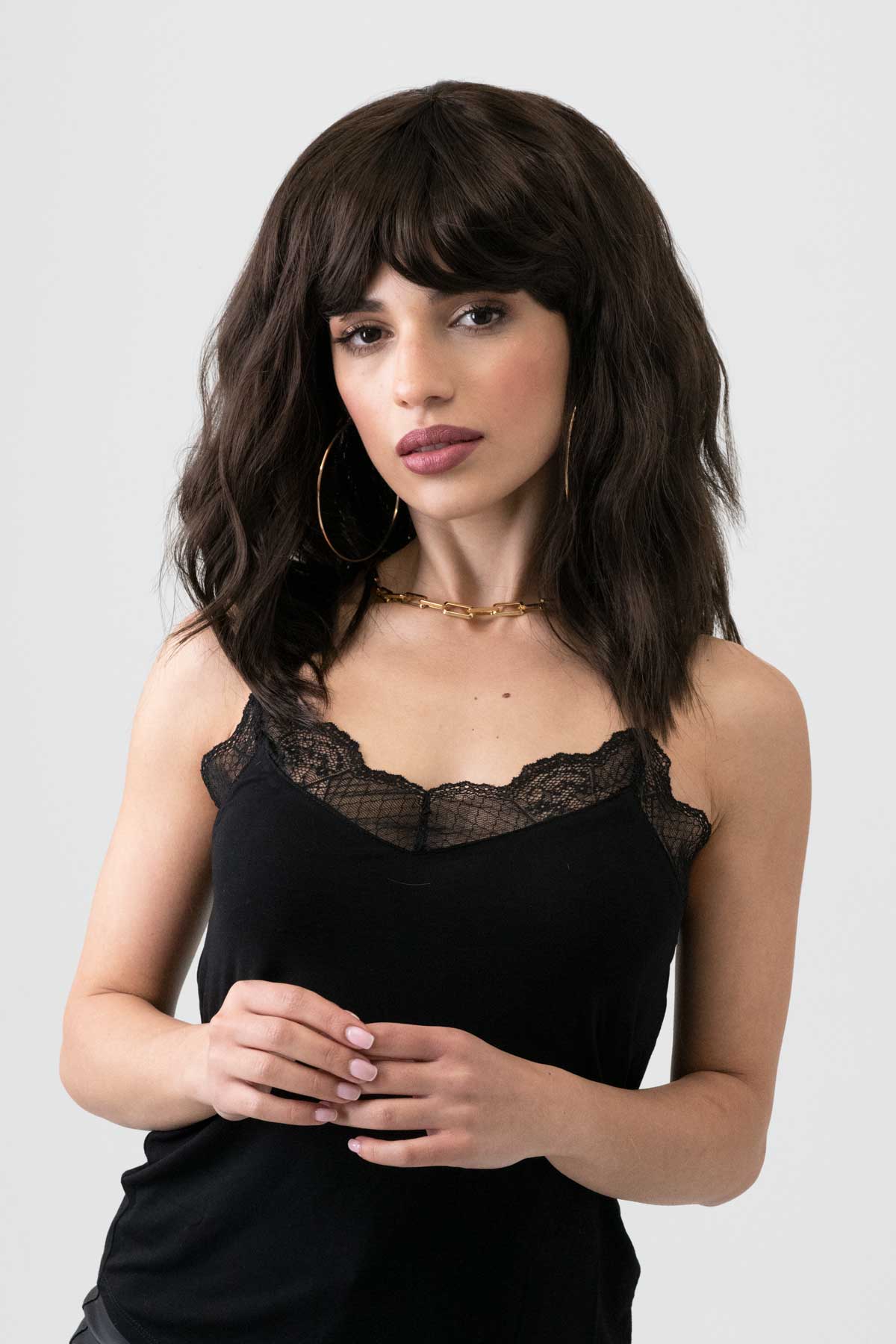 Woman wearing a black lace top against a plain background. Dark chocolate brown long wavy bob wig: Roxy