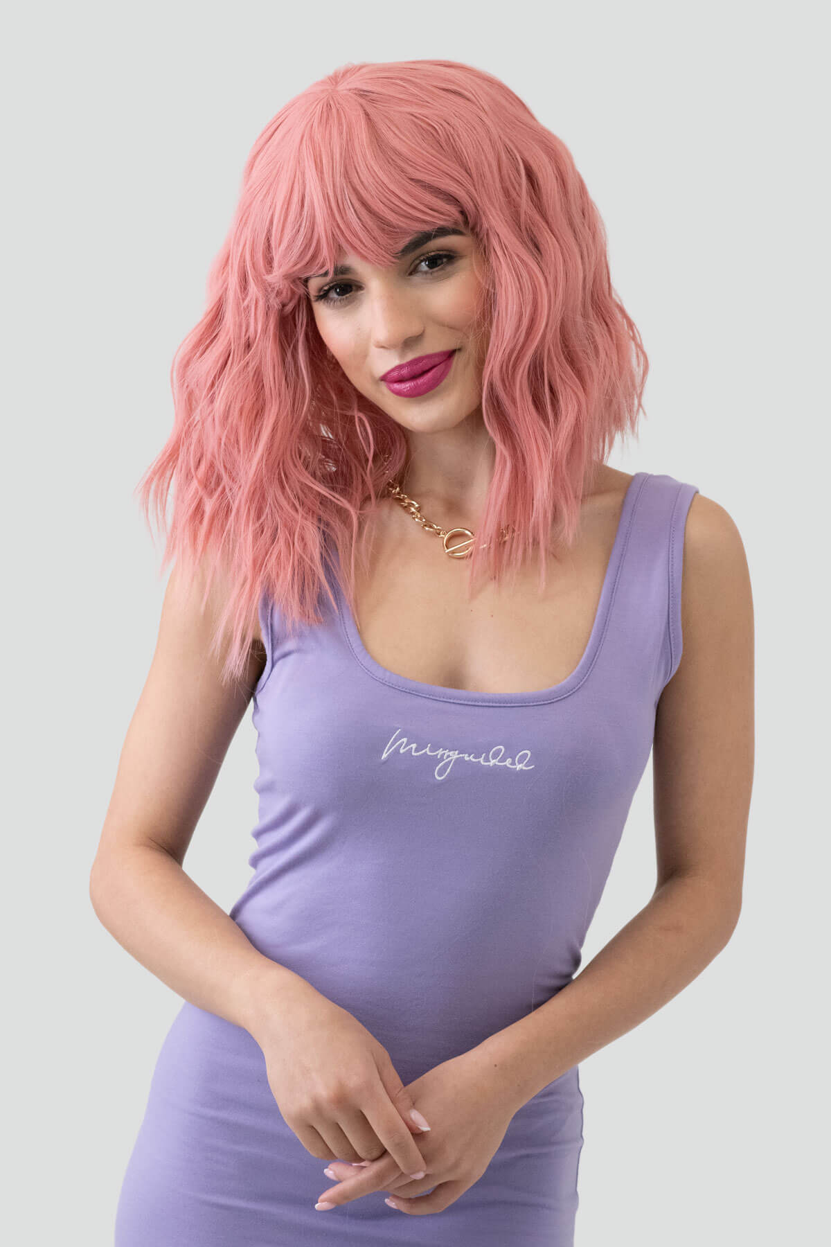 Woman with pink wig wearing a purple tank top with text on a light gray background. Dusty pink long wavy bob wig (LOB) with textured waves: Fearne