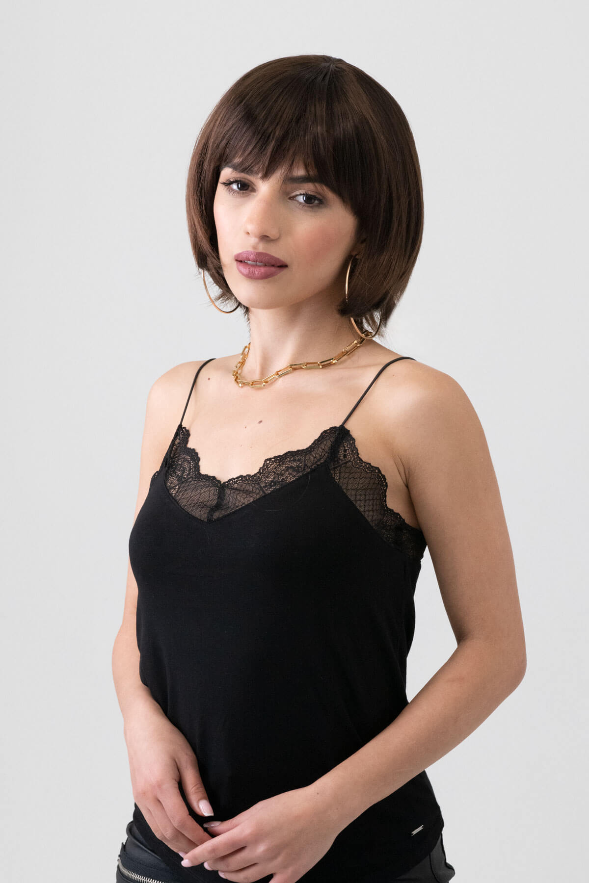 Woman wearing a black lace camisole against a plain background. Dark brown pixie cut wig with reddish brown lowlights: Cierra