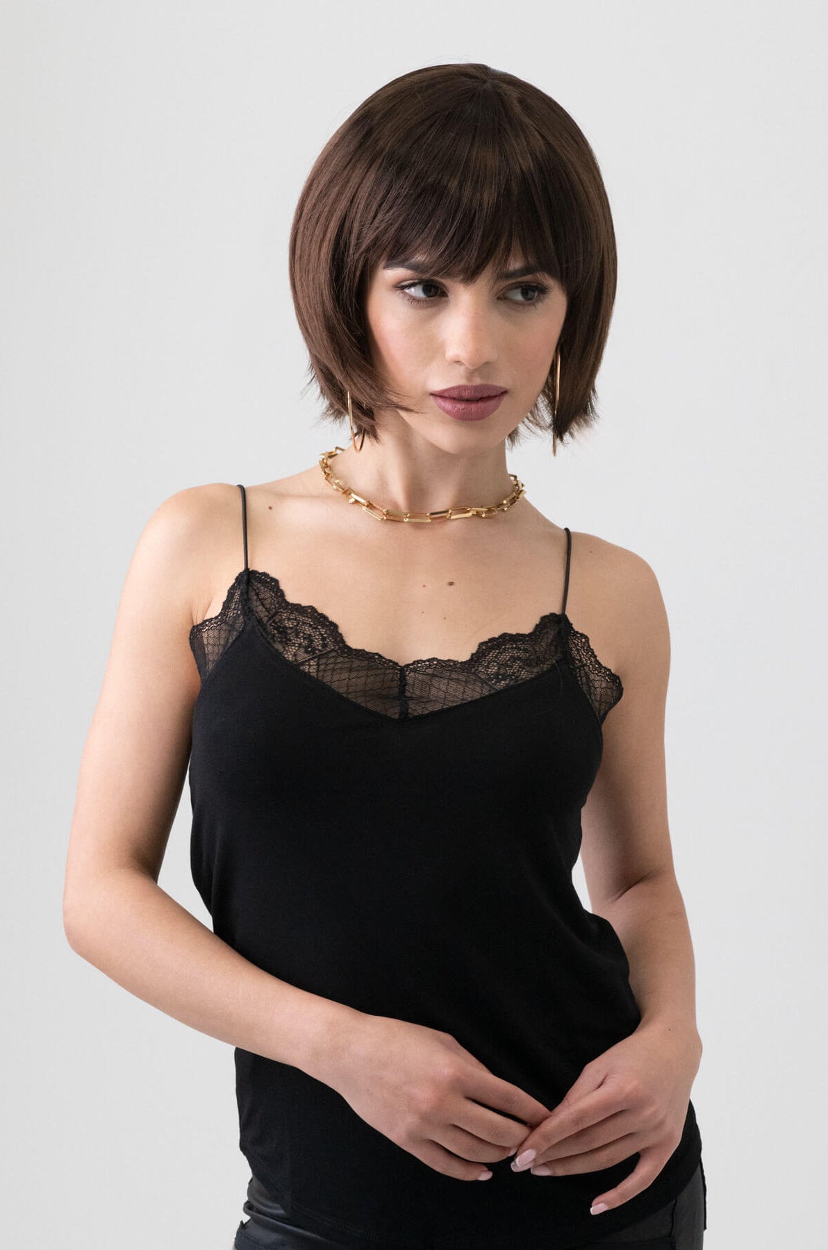 Woman wearing a black lace camisole against a plain background. Dark brown pixie cut wig with reddish brown lowlights: Cierra