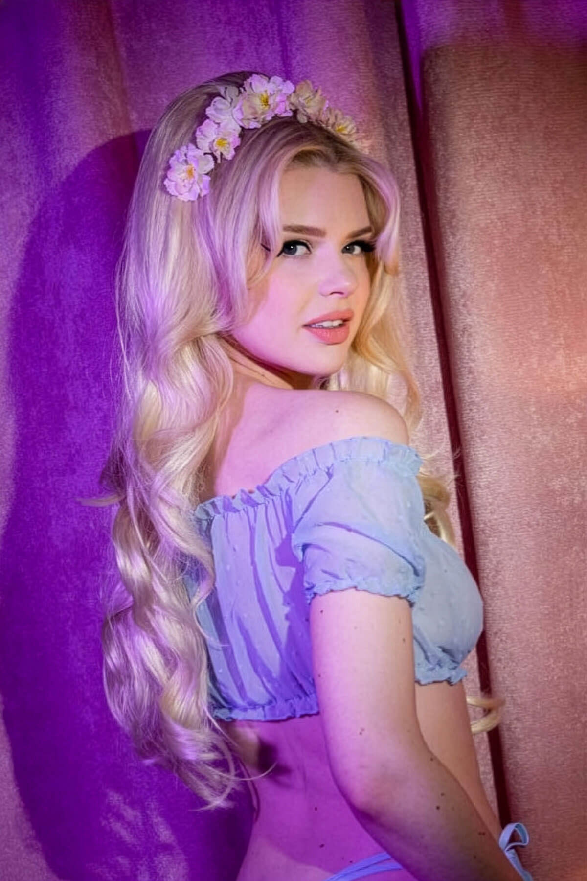 Woman with floral headband and off-shoulder top against a pink and purple curtain. High crown long, wavy half wig and volume ring blonde: Bardot blonde 613t24