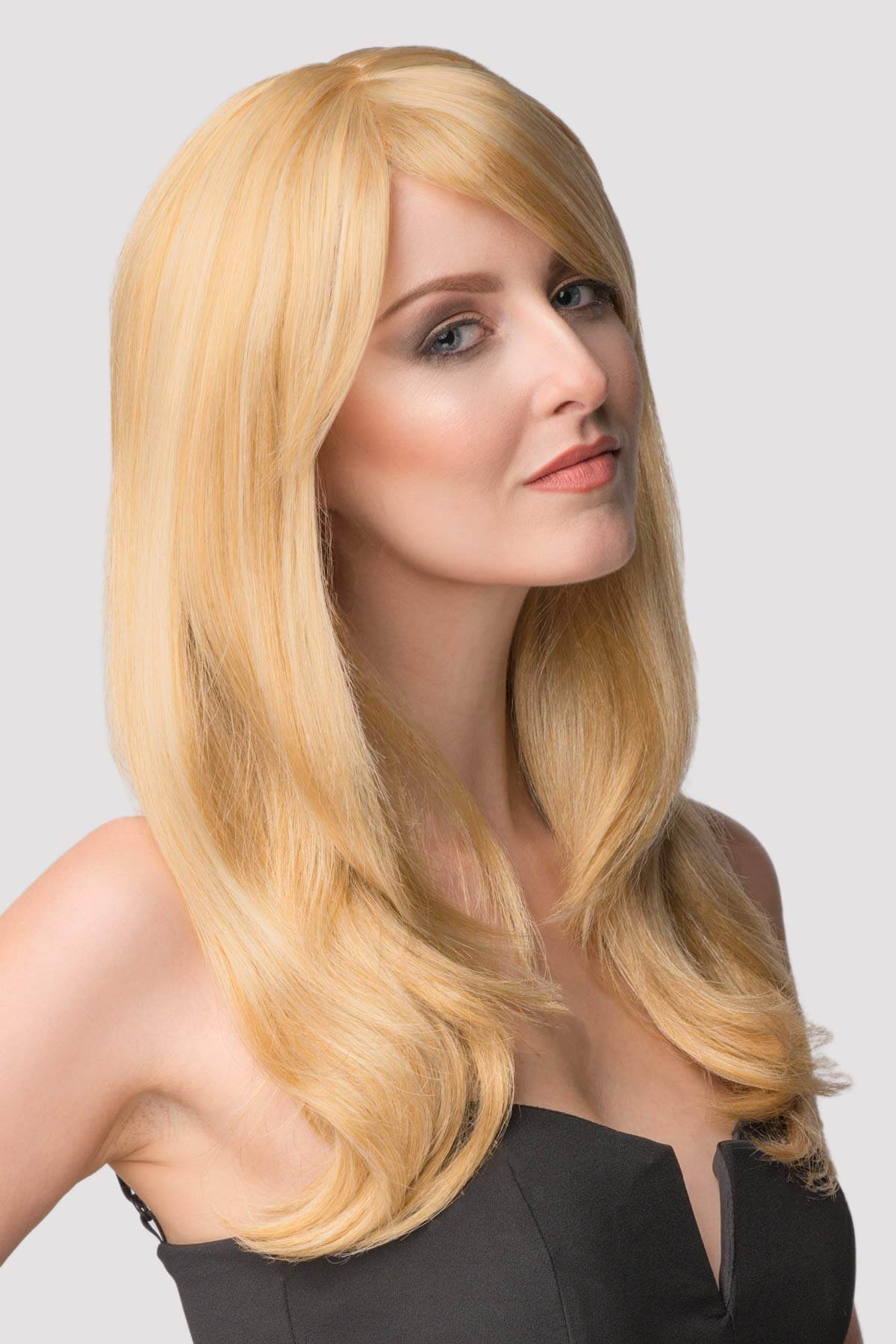 Woman with long blonde wig on a plain background. Long blonde wig, face framing with long, side-sweeping fringe: Ashley honey blonde 24BH613