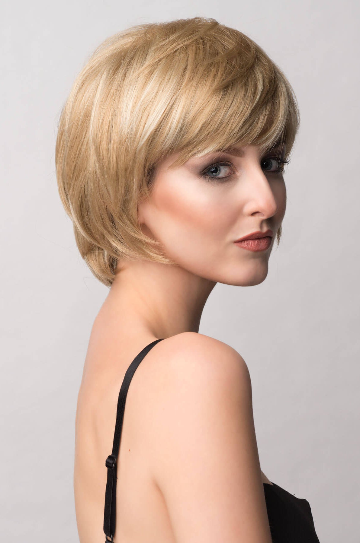 Woman with a stylish haircut against a plain background. Pixie cut wig, layered and short: Sophia