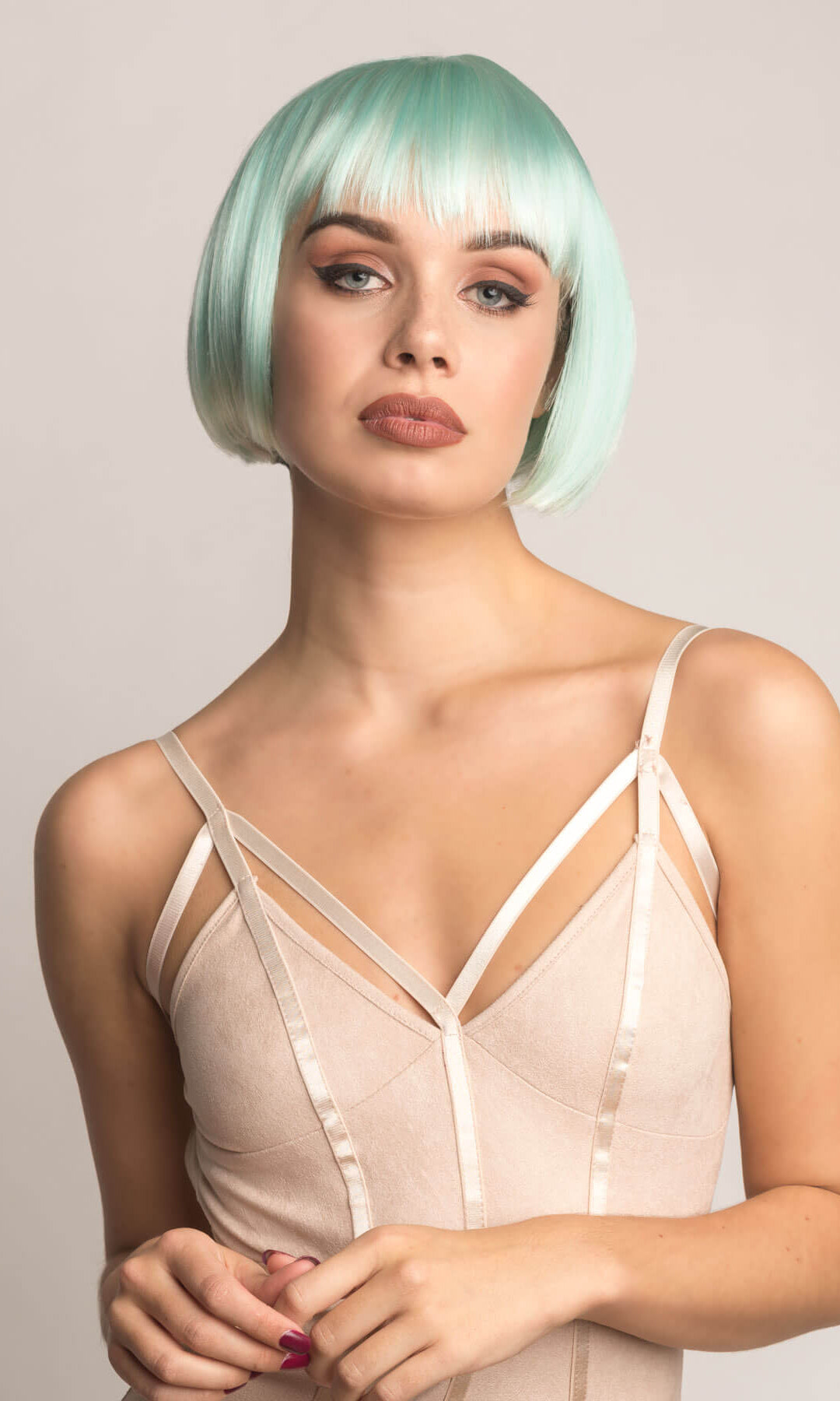 Woman with a stylish haircut wearing a beige satin dress against a plain background. Turquoise bob wig, with platinum blonde ombre, short and chic: Eunice