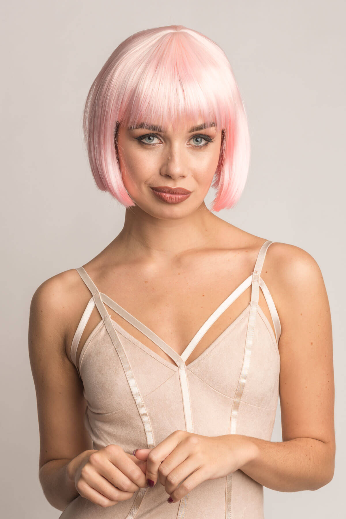 Woman with pink bob wig wearing a beige strappy top against a plain background. Short pink bob wig (ombre: pale pink and platinum): Louisa