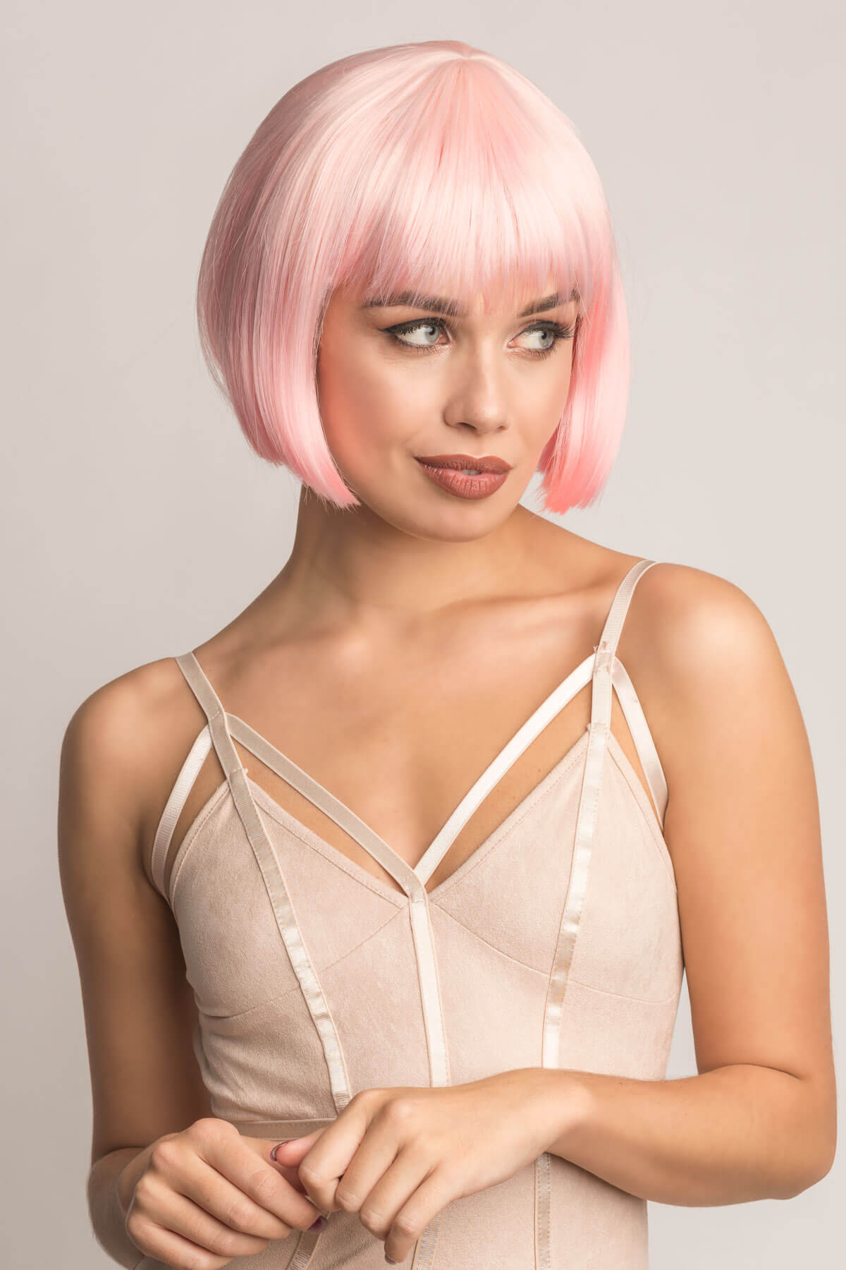 Woman with pink bob wig wearing a beige strappy top against a plain background. Short pink bob wig (ombre: pale pink and platinum): Louisa