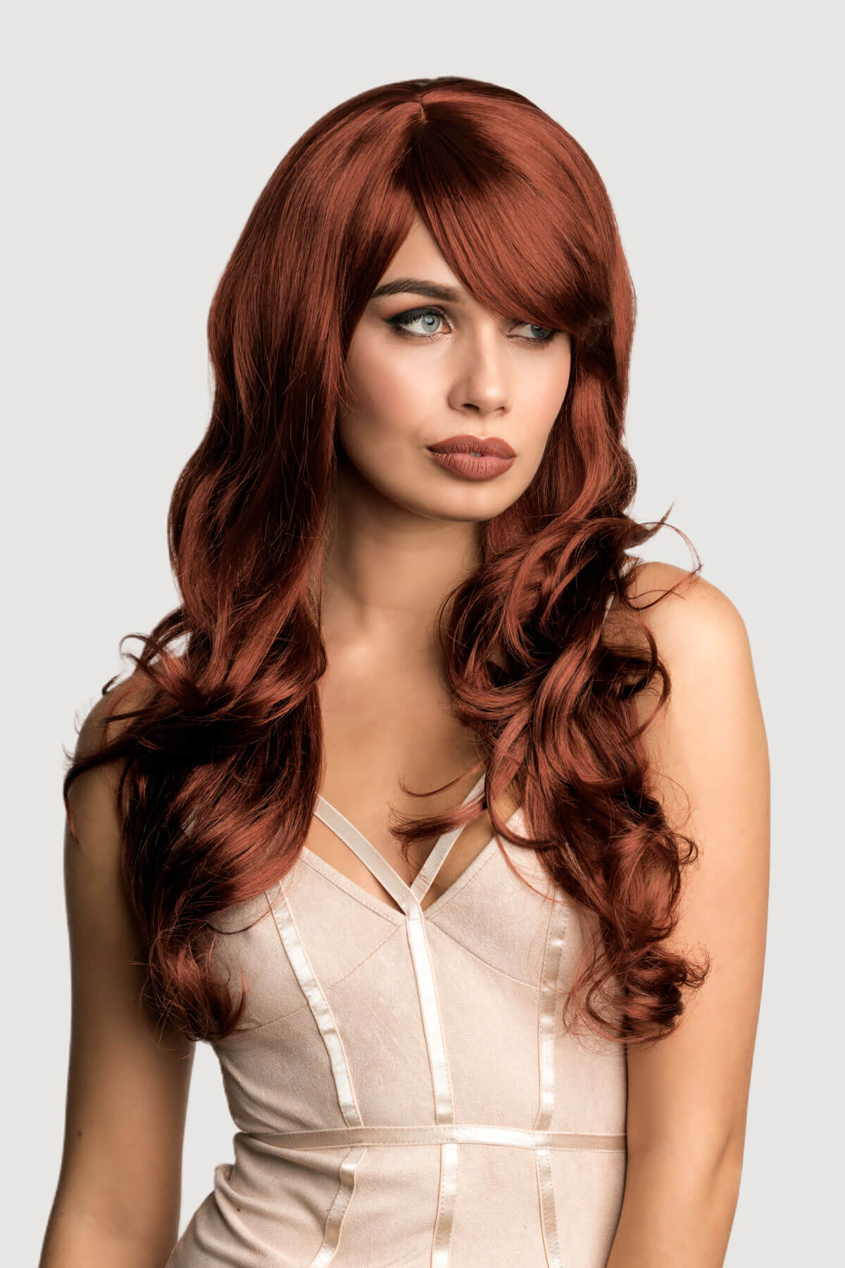 Woman with long, wavy red hair wearing a beige dress against a light gray background. Long copper red wig with gentle waves: Kelly