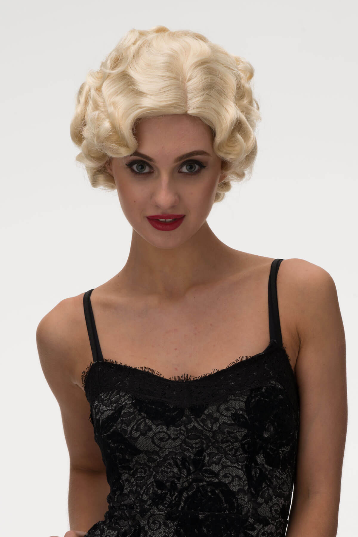 Woman wearing a blonde wig and black lace dress on a white background. Blonde 1920s 1930s style wig, short with finger waves: Diva champagne blonde 613