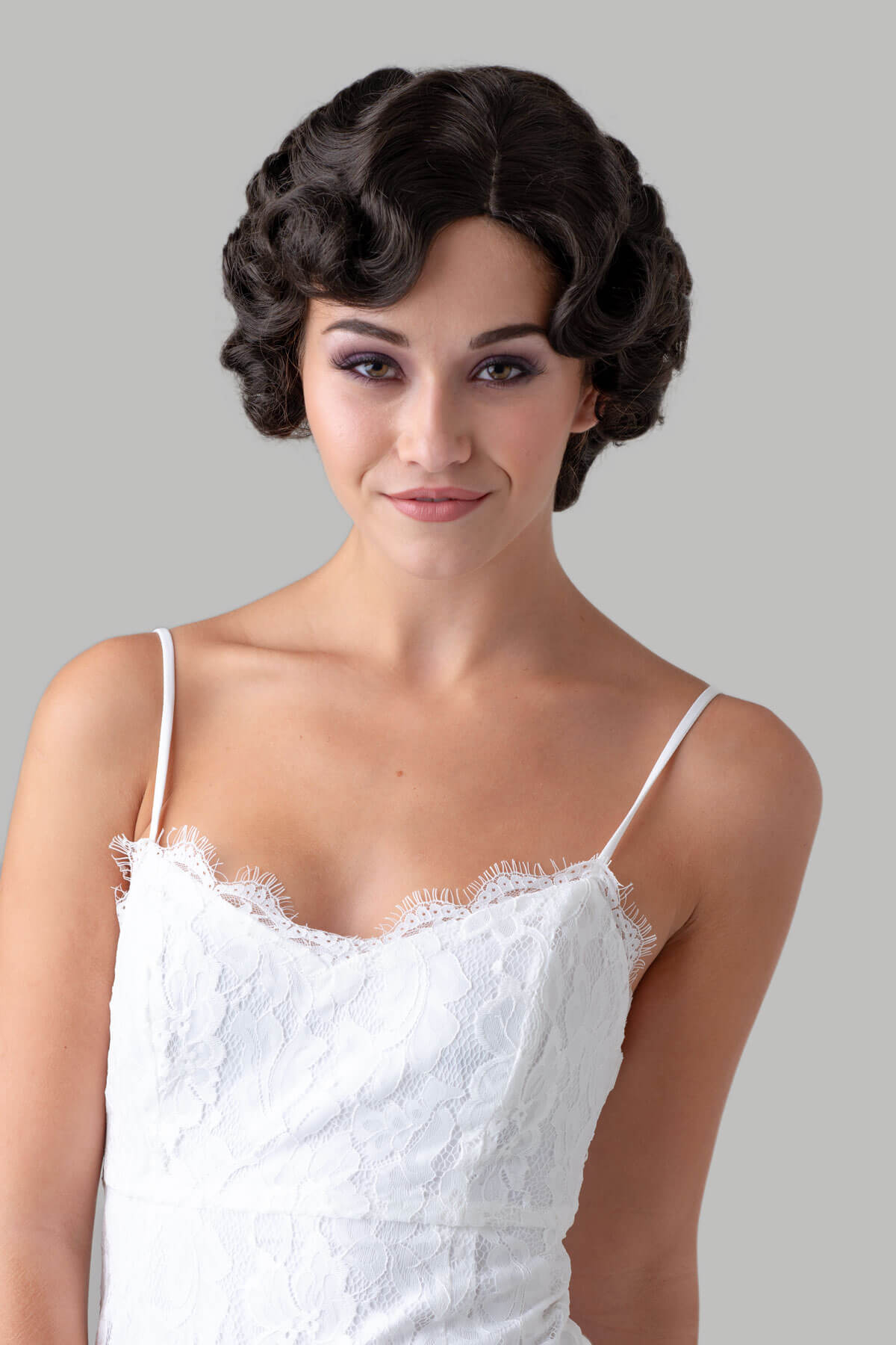 Woman wearing a white lace dress with a gray background. Brown 1920s 1930s style wig, short retro style with finger waves: Cecelia dark drown 4
