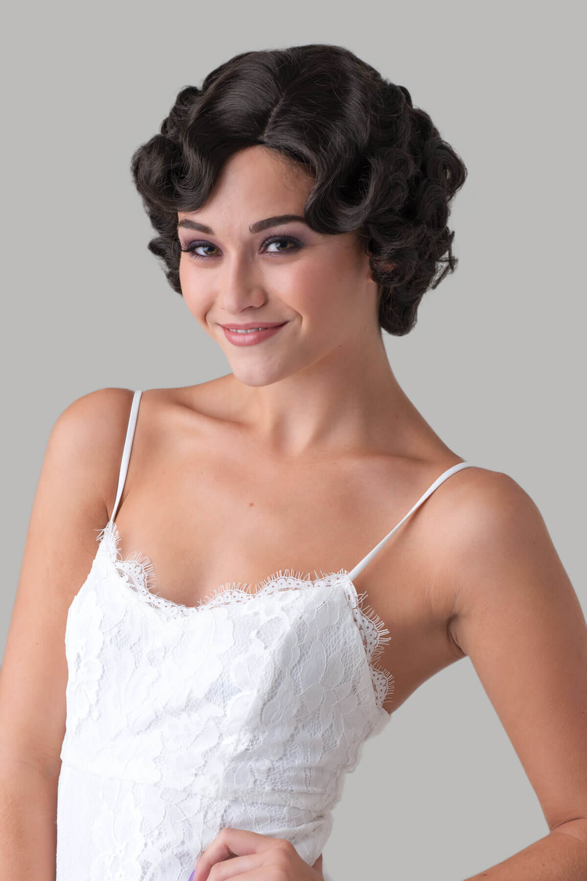 Woman wearing a white lace dress with a gray background. Brown 1920s 1930s style wig, short retro style with finger waves: Cecelia dark drown 4