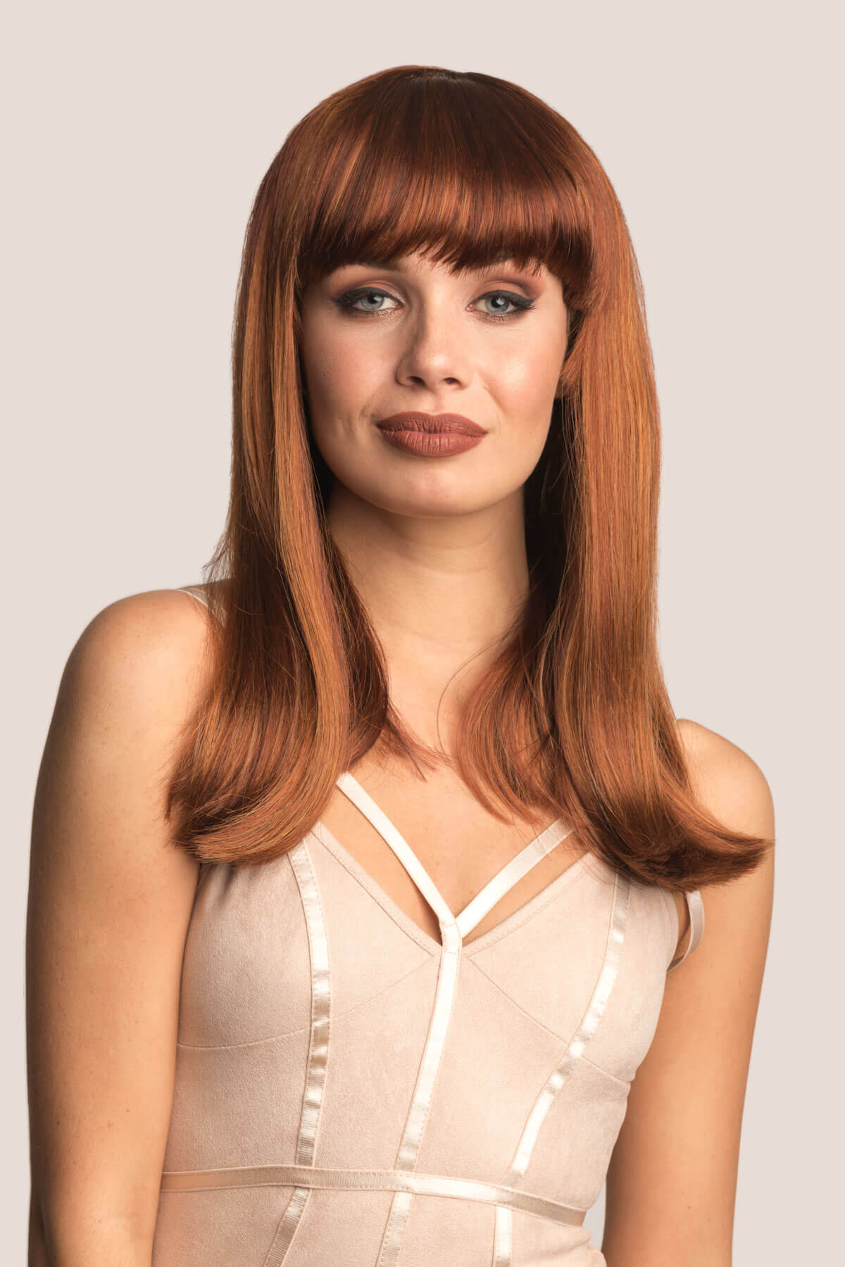 Woman with long brown hair wearing a beige dress against a plain background. Red/Auburn wig with blonde highlights and straight fringe: Abi