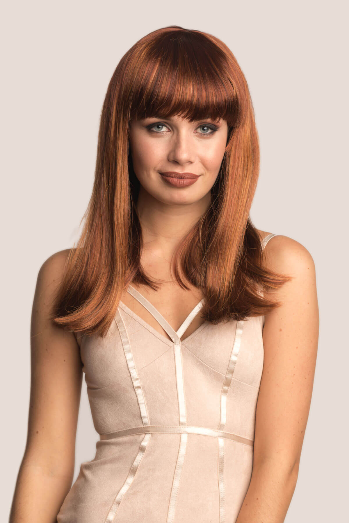 Woman with long brown hair wearing a beige dress against a light background. Red/Auburn wig with blonde highlights and straight fringe: Abi