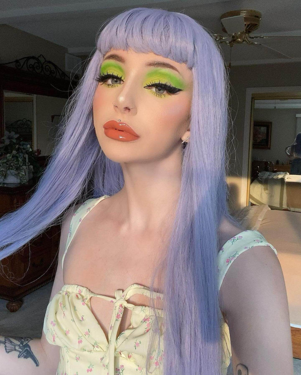 Person with purple hair and green makeup in a room setting. Long blue wig with short, straight fringe: Alyssa